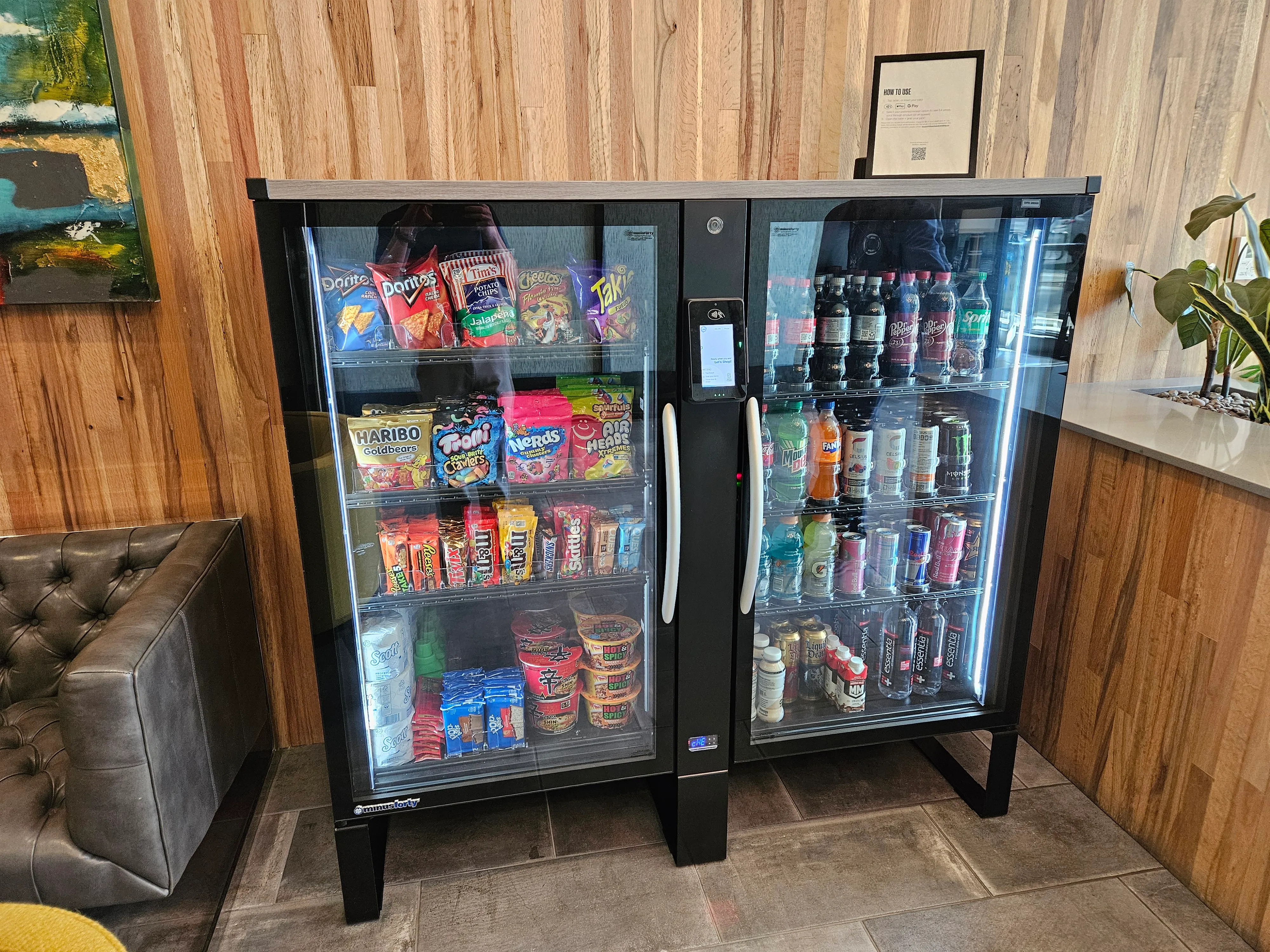 Modern community market with well-stocked refrigerated drinks and snacks section, stylish interior design, and convenient self-checkout kiosk.