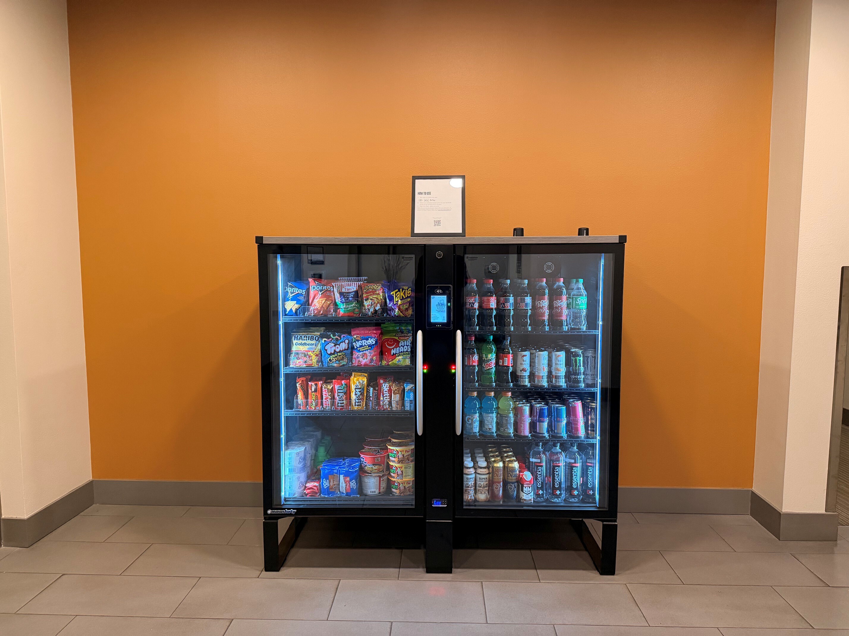 Modern vending machine well-stocked with a variety of snacks and drinks against a stylish orange wall.