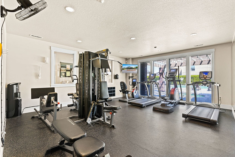 Bright and modern fitness center with state-of-the-art gym equipment, including treadmills and strength training machines, overlooking a serene outdoor pool area.