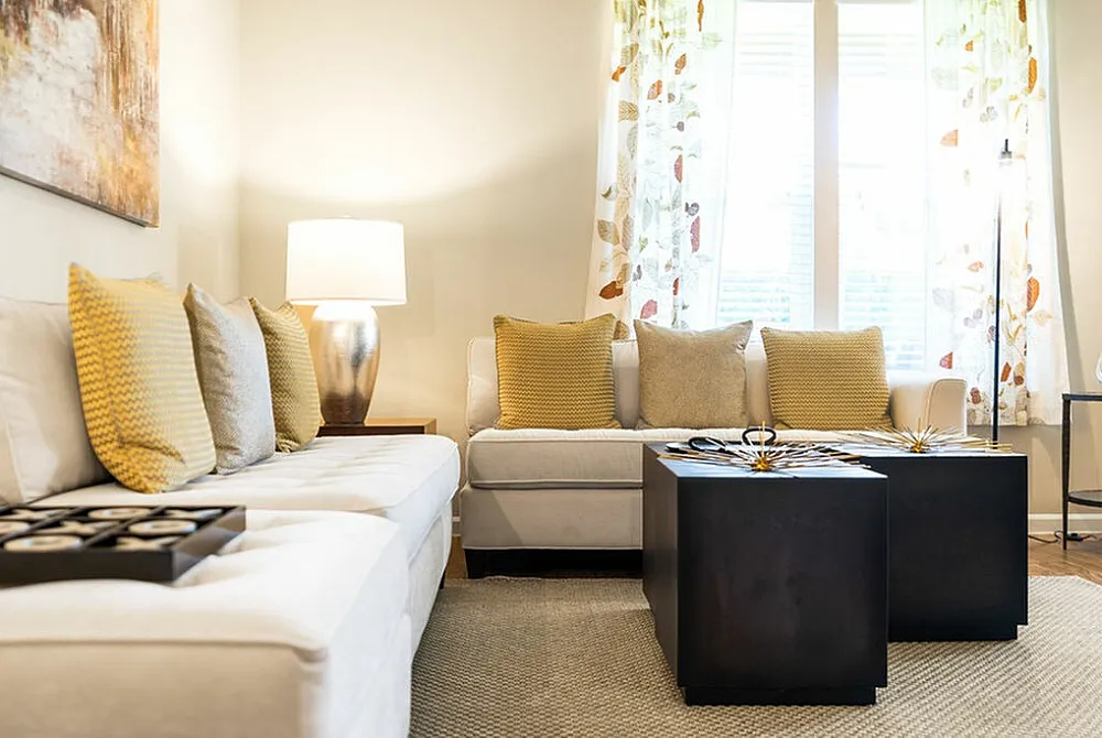 Inviting living room with elegant beige sofas, stylish yellow cushions, and modern decor, illuminated by natural light through large windows.