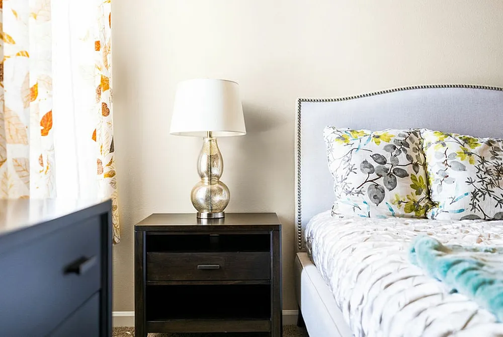 Cozy bedroom with elegant bedside lamp, floral-patterned pillows, and soothing natural light.
