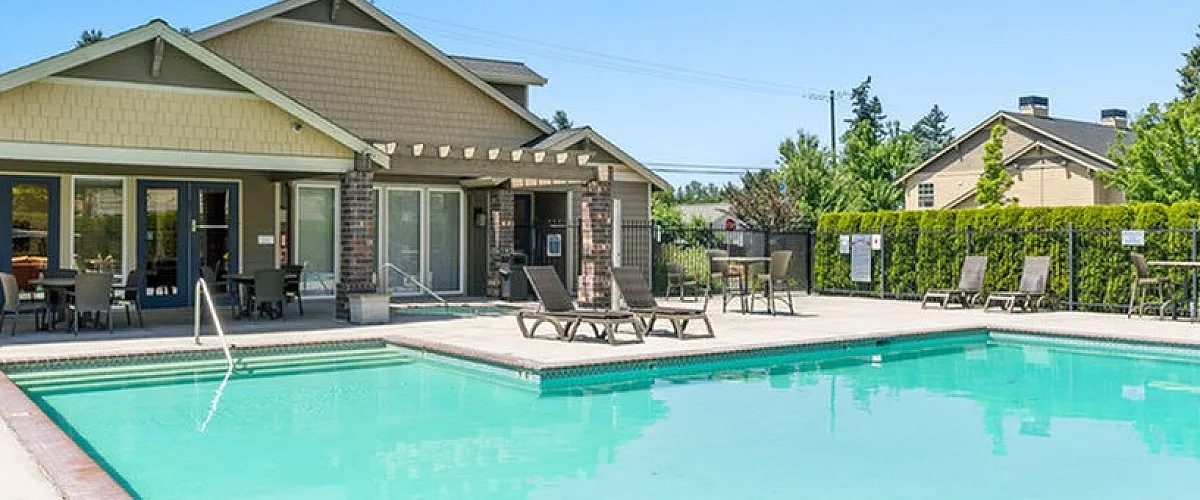 Inviting community swimming pool with sun loungers and a charming clubhouse, perfect for relaxing and socializing on a sunny day.