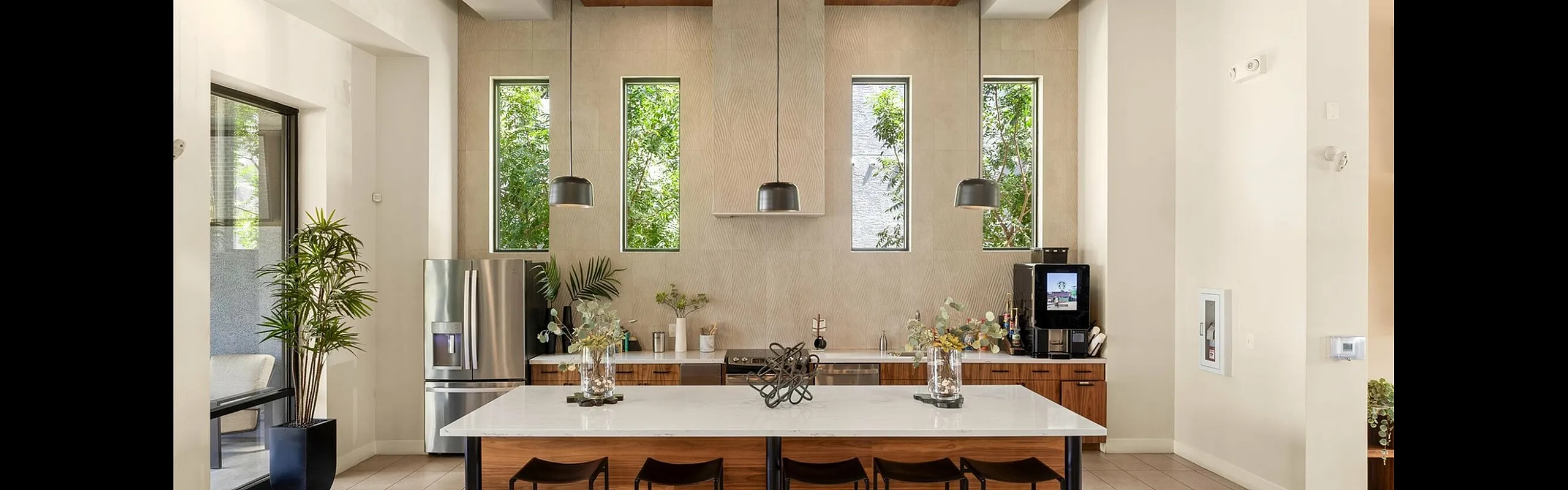 Modern kitchen with sleek design features a large island with seating, stylish pendant lighting, stainless steel appliances, and lush greenery for a fresh and inviting atmosphere.