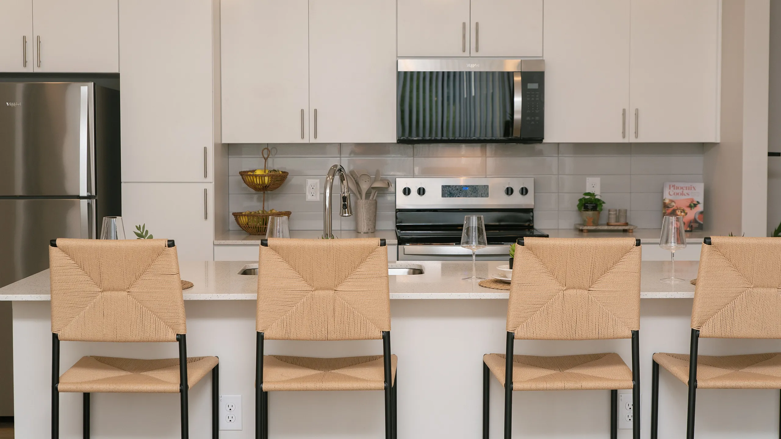 Modern kitchen with sleek white cabinetry, stainless steel appliances, and chic bar seating under elegant pendant lighting.