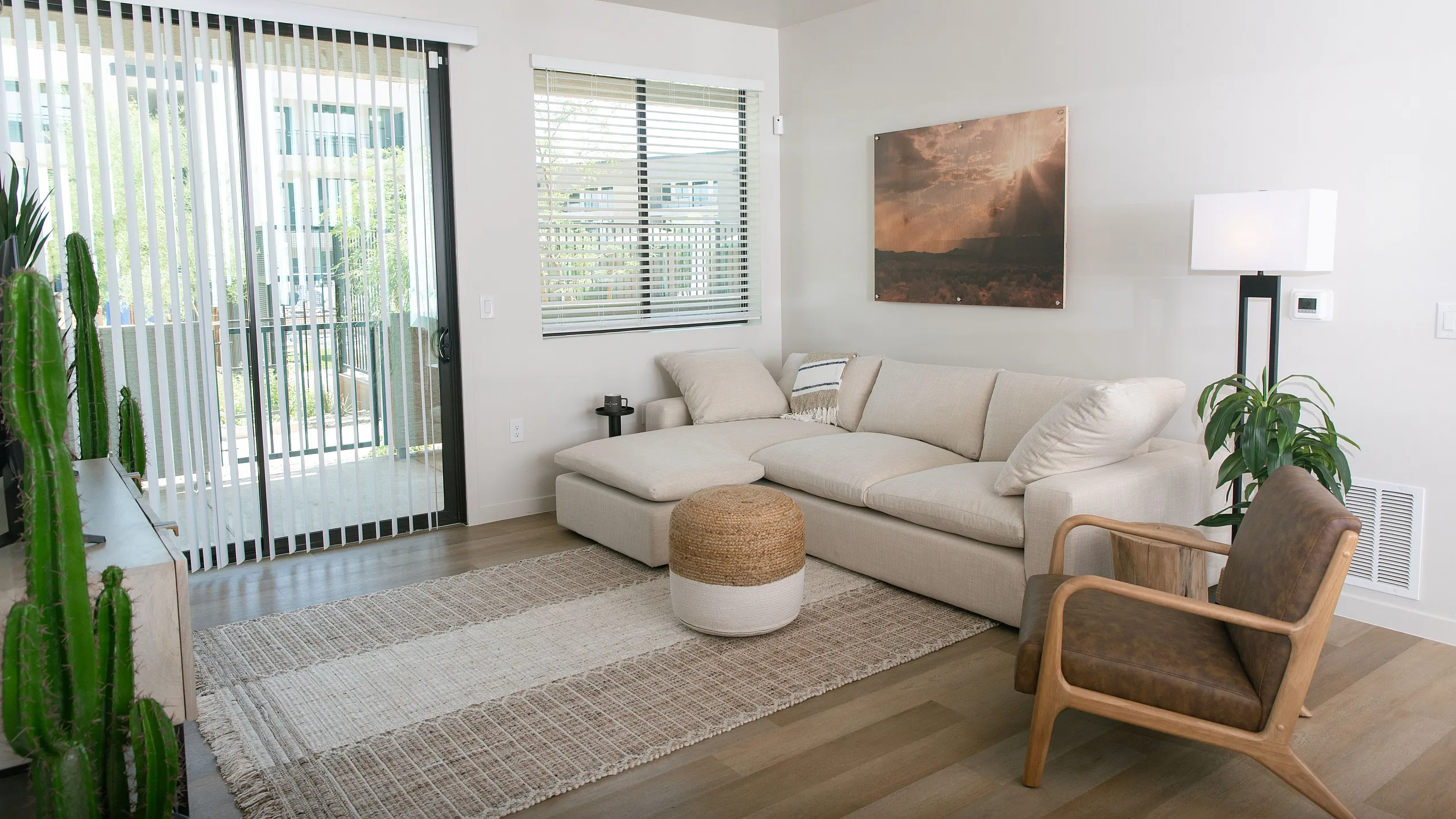 Bright living room with modern decor, featuring a cozy beige sectional, stylish armchair, and natural accents like plants and woven textures, perfect for relaxation.