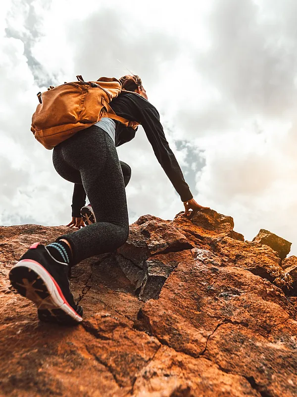 Adventurous hiker climbing rocky terrain under a dramatic sky, capturing the essence of exploration and outdoor freedom.
