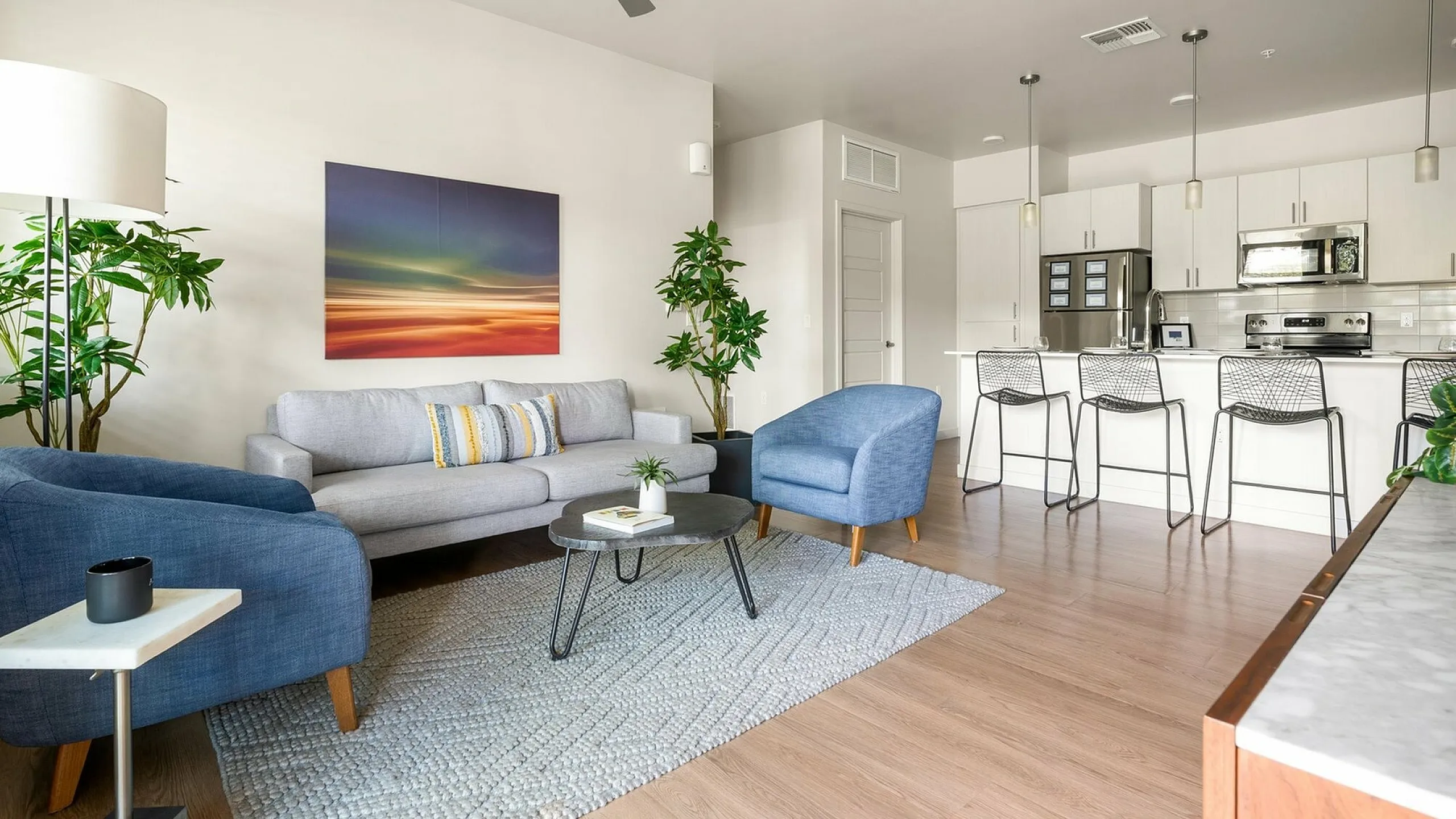 Modern open-concept living space showcasing a cozy seating area with contemporary furniture, vibrant artwork, and a sleek kitchen with bar seating.