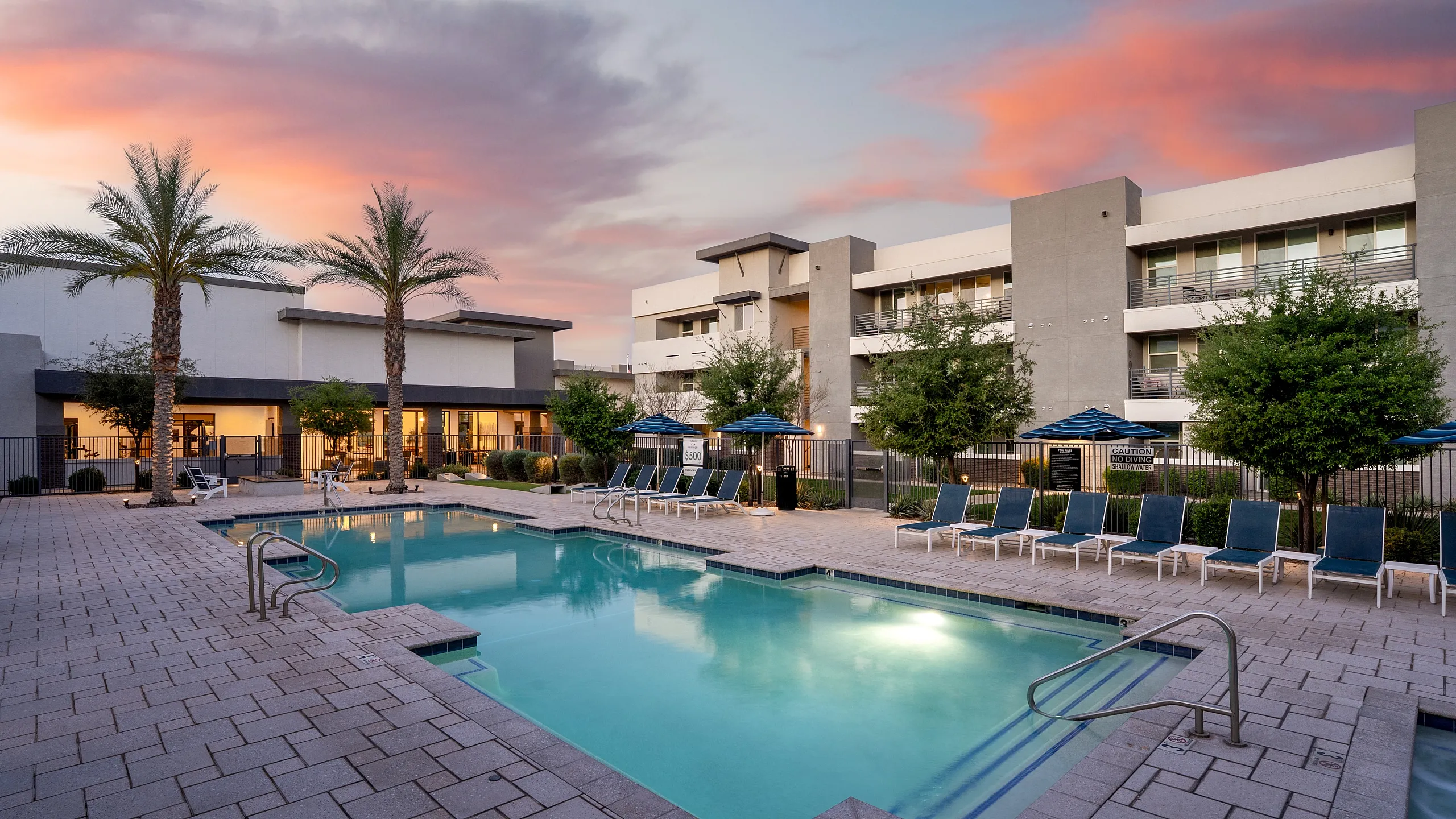 Luxurious apartment complex showcasing a sparkling pool surrounded by elegant lounge chairs under a stunning sunset.