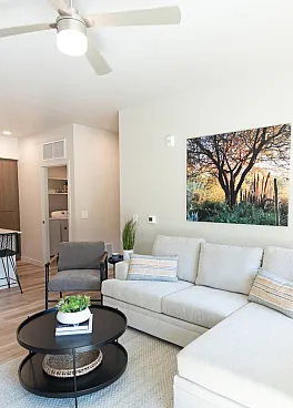 Bright and modern living room at Acero Harvest Station apartments with cozy sectional sofa, stylish coffee table, and nature-inspired wall art, perfect for relaxation.