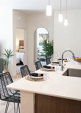 Chic apartment in queen creek az with kitchen with stylish pendant lighting, featuring a sleek island and elegant dining setup, opening to a cozy bedroom.