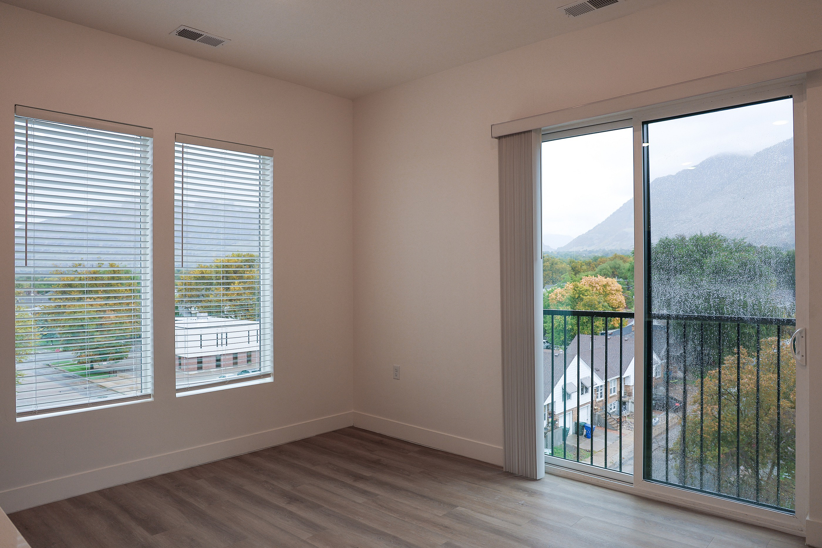 Bright and airy room with large windows and a sliding glass door leading to a scenic balcony view.