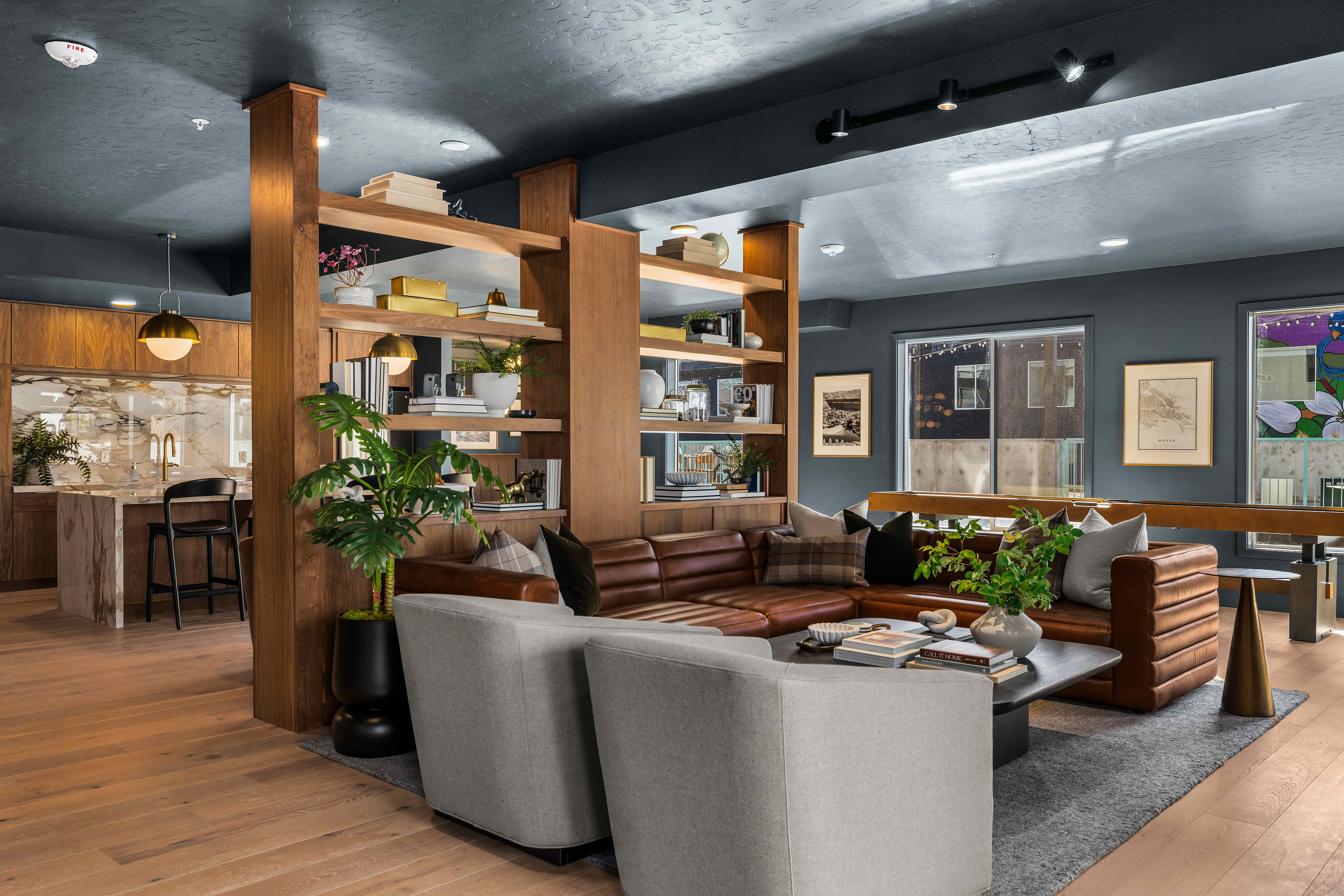 Chic open-concept living area featuring a leather sectional sofa, modern shelving with decor, and elegant kitchen, bathed in natural light.