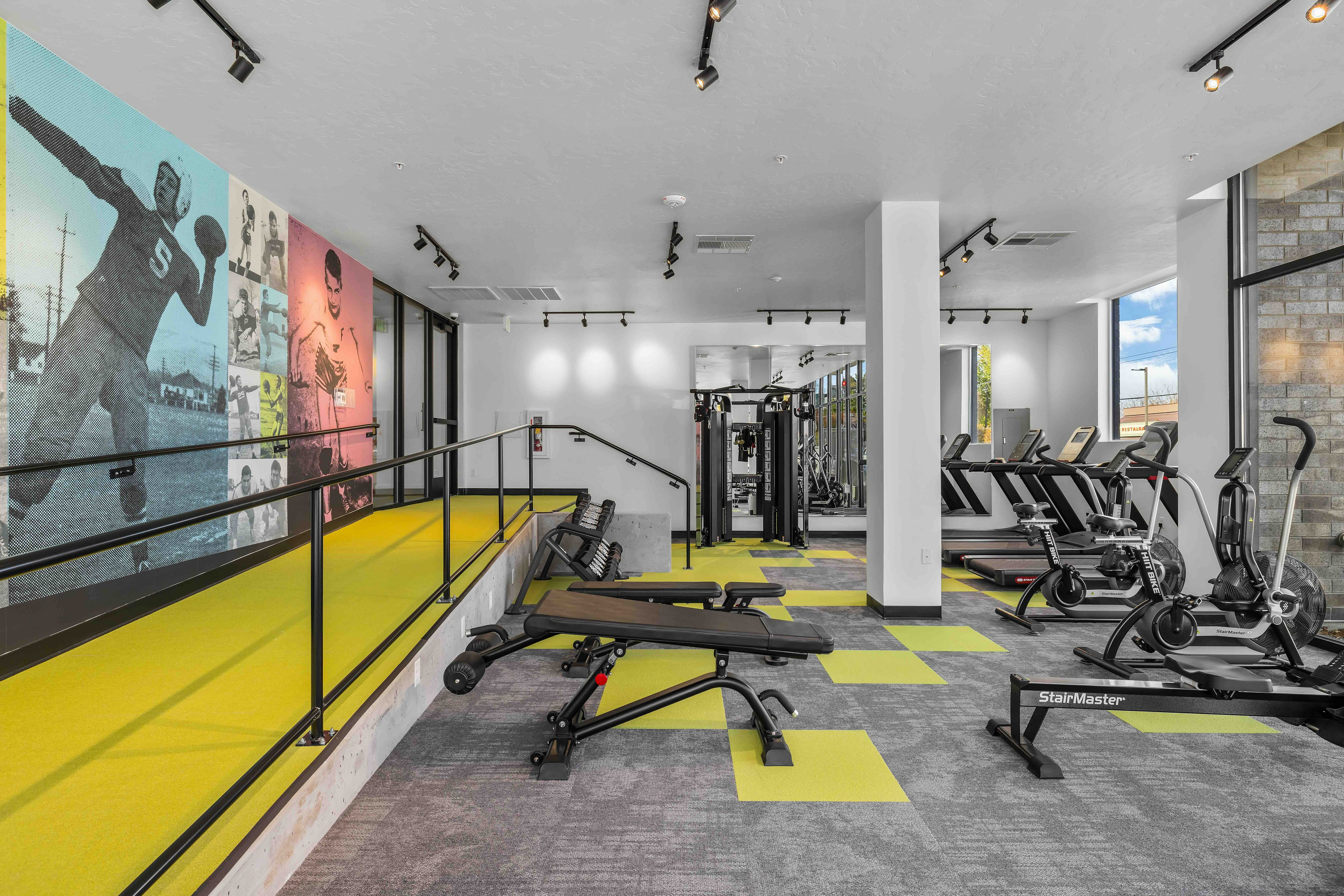 Modern fitness center with vibrant art mural, featuring state-of-the-art exercise machines, comfortable seating, and large windows for natural light.