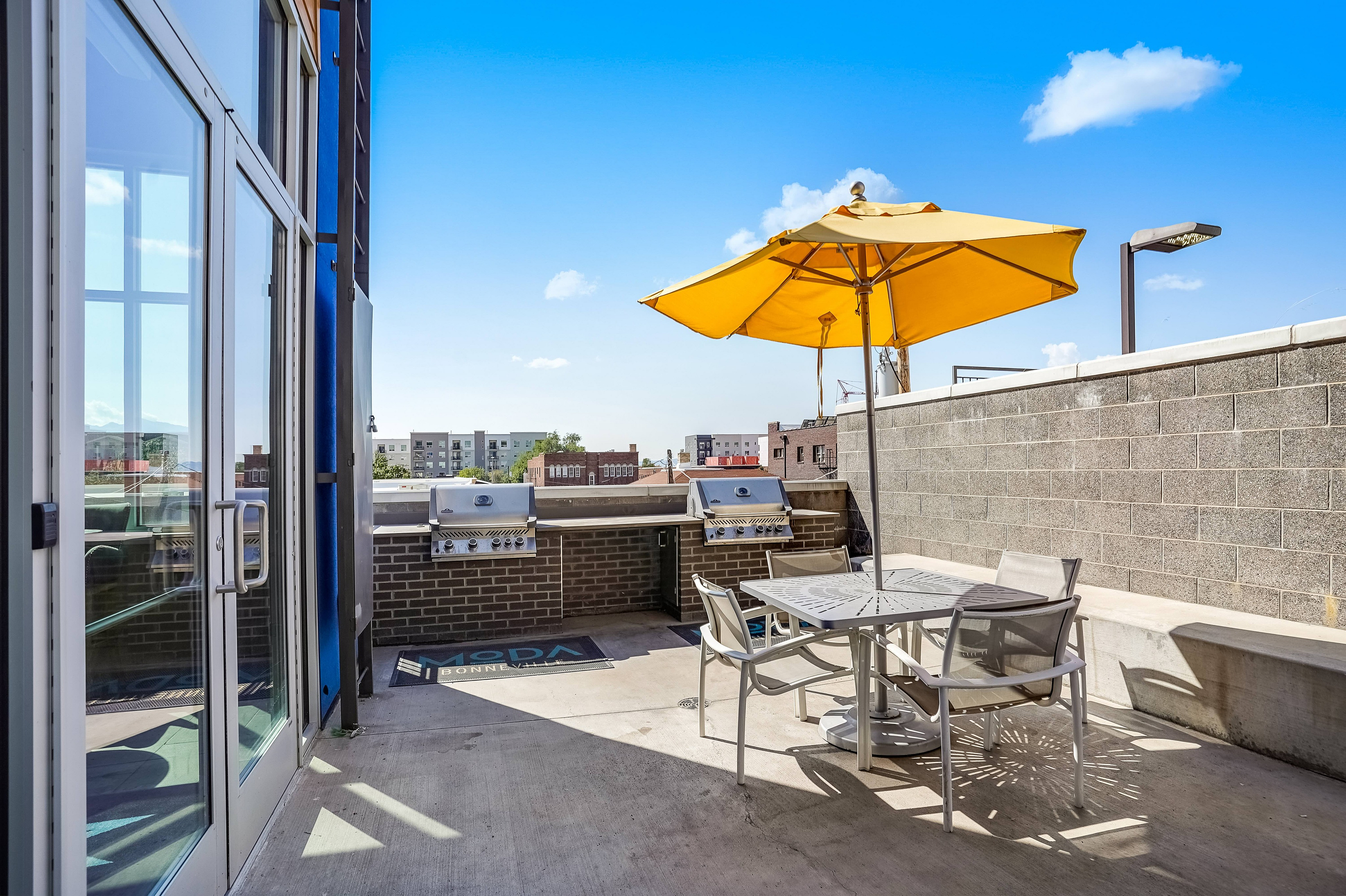 Chic urban patio with modern furniture, vibrant yellow umbrella, and dual stainless steel grills perfect for entertaining.