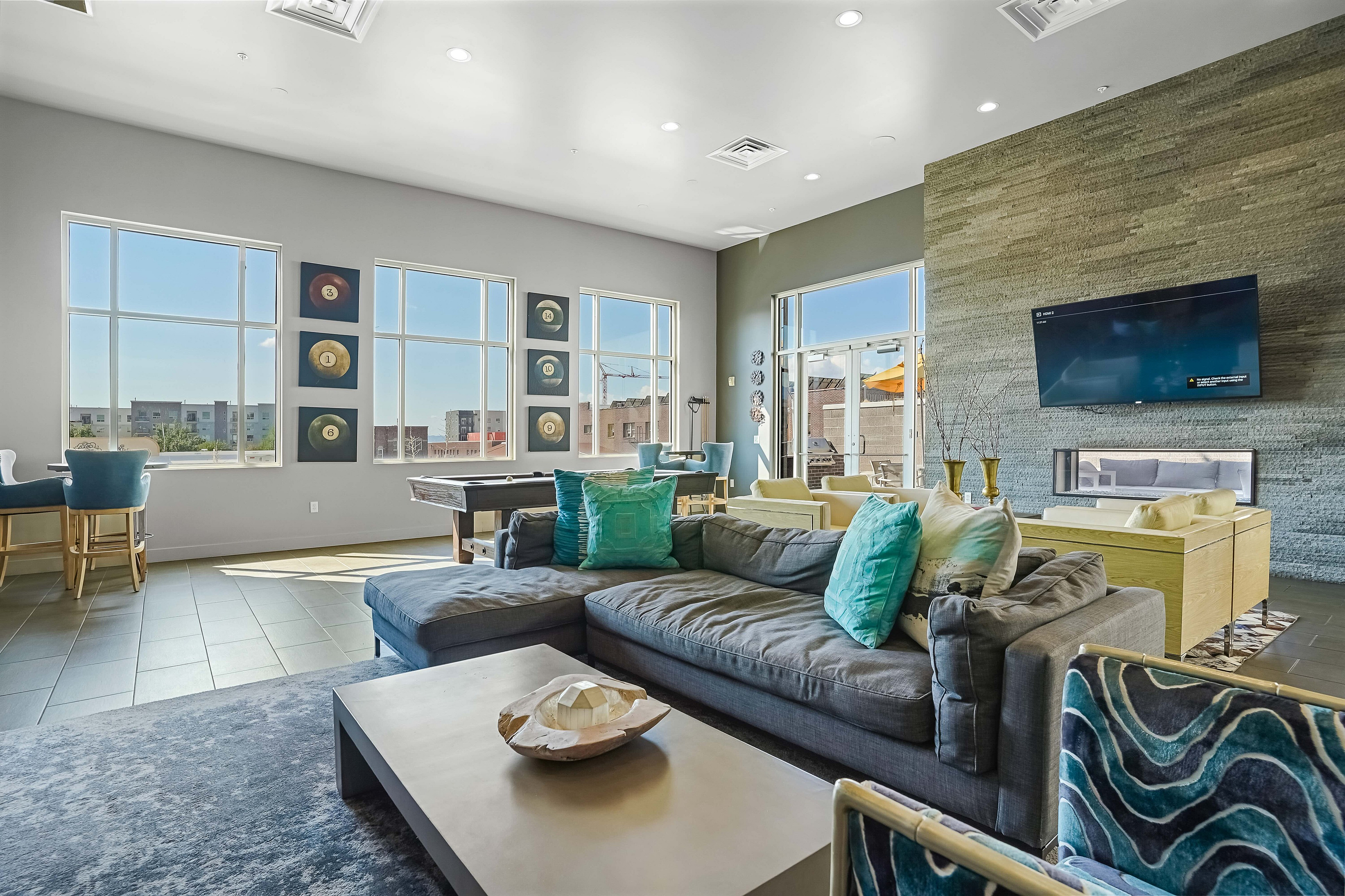Bright and spacious living room with modern decor, featuring large windows, a comfortable sectional sofa, and a wall-mounted TV.