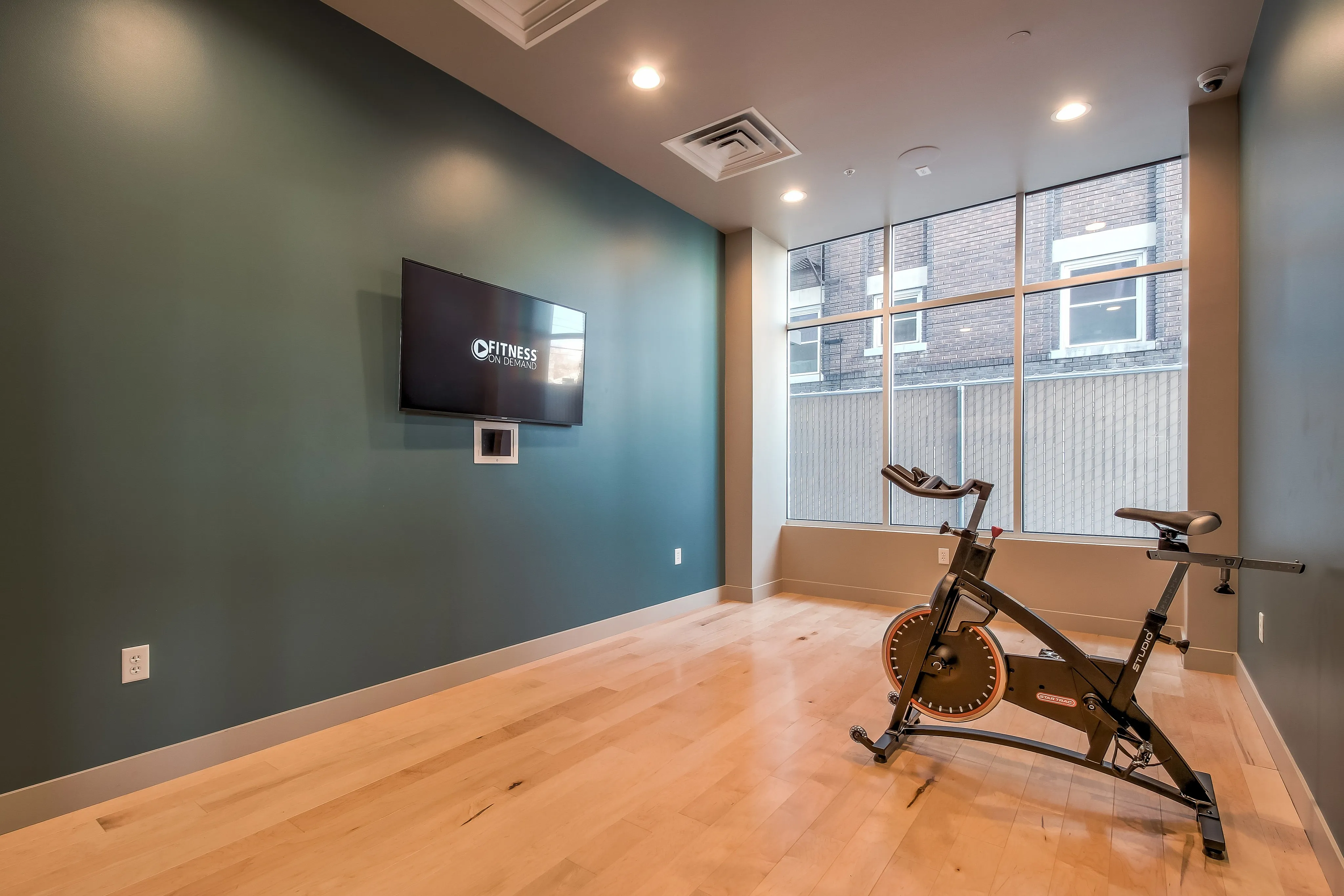 Contemporary fitness room with a sleek stationary bike, large window for natural light, and a wall-mounted screen for virtual workouts.