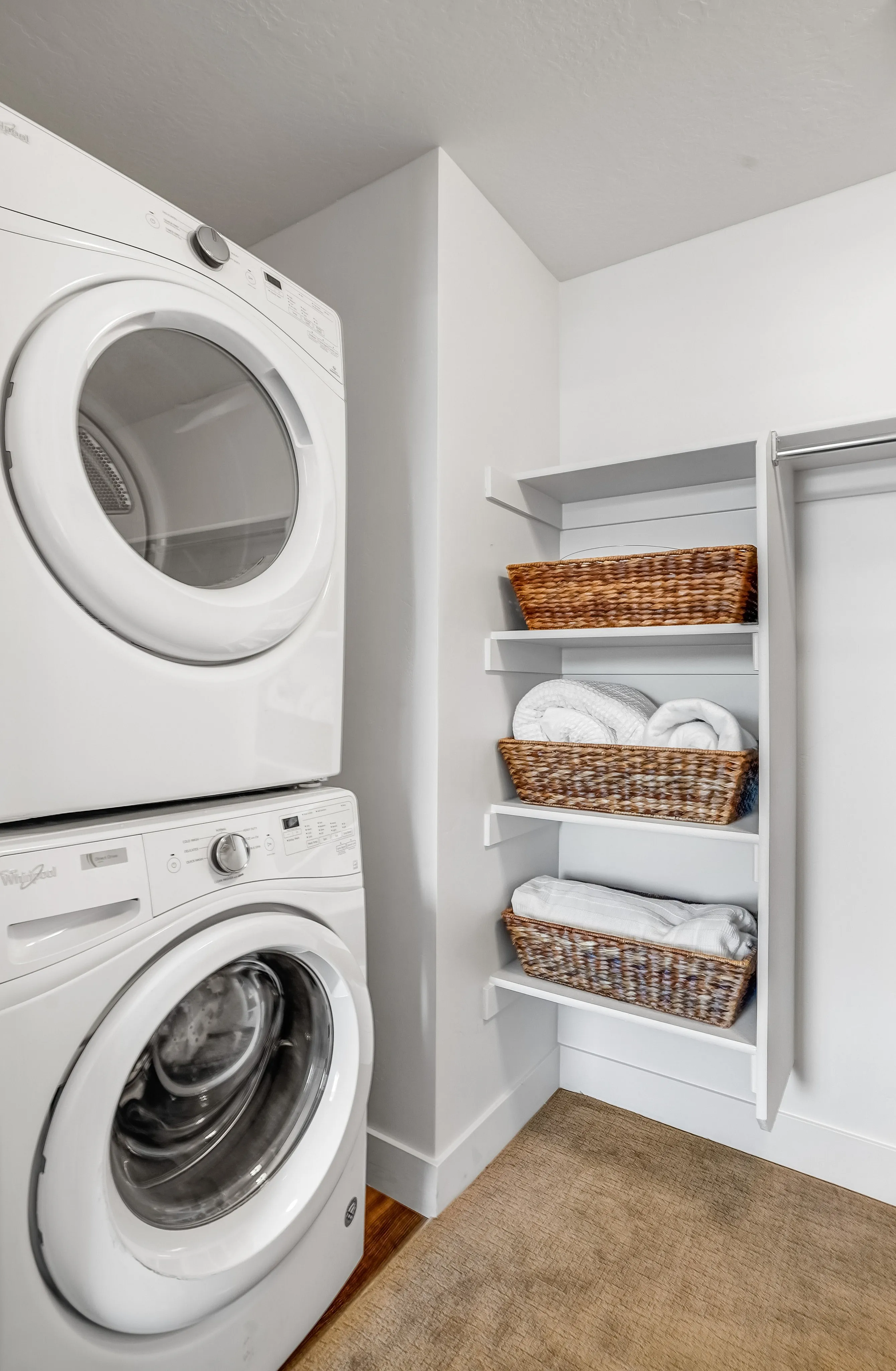 Elegant laundry room with a modern stackable washer and dryer, complemented by stylish wicker baskets on open shelves for a functional and organized space.