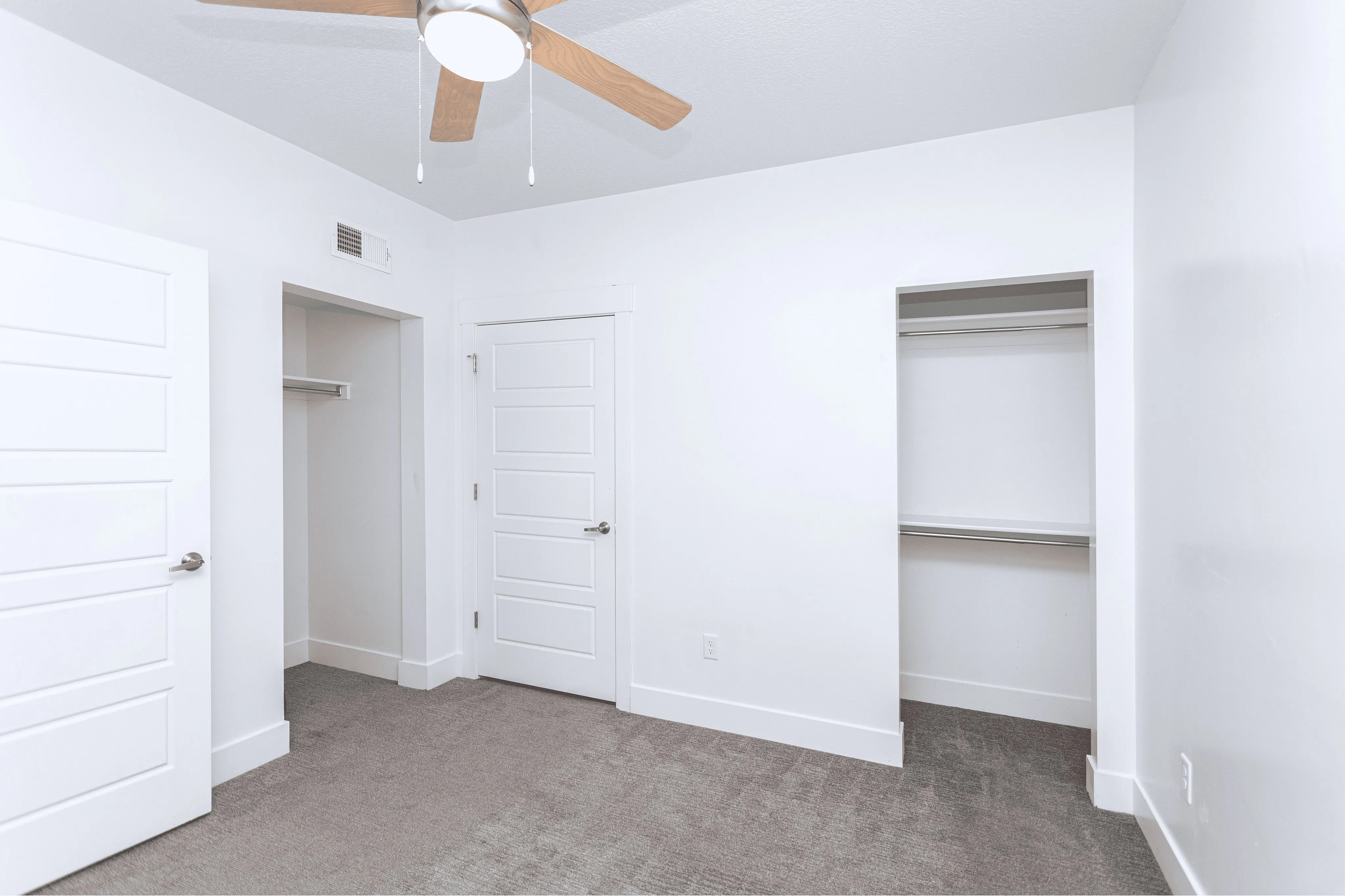 Bright bedroom with modern ceiling fan, dual closet space, and elegant white doors.