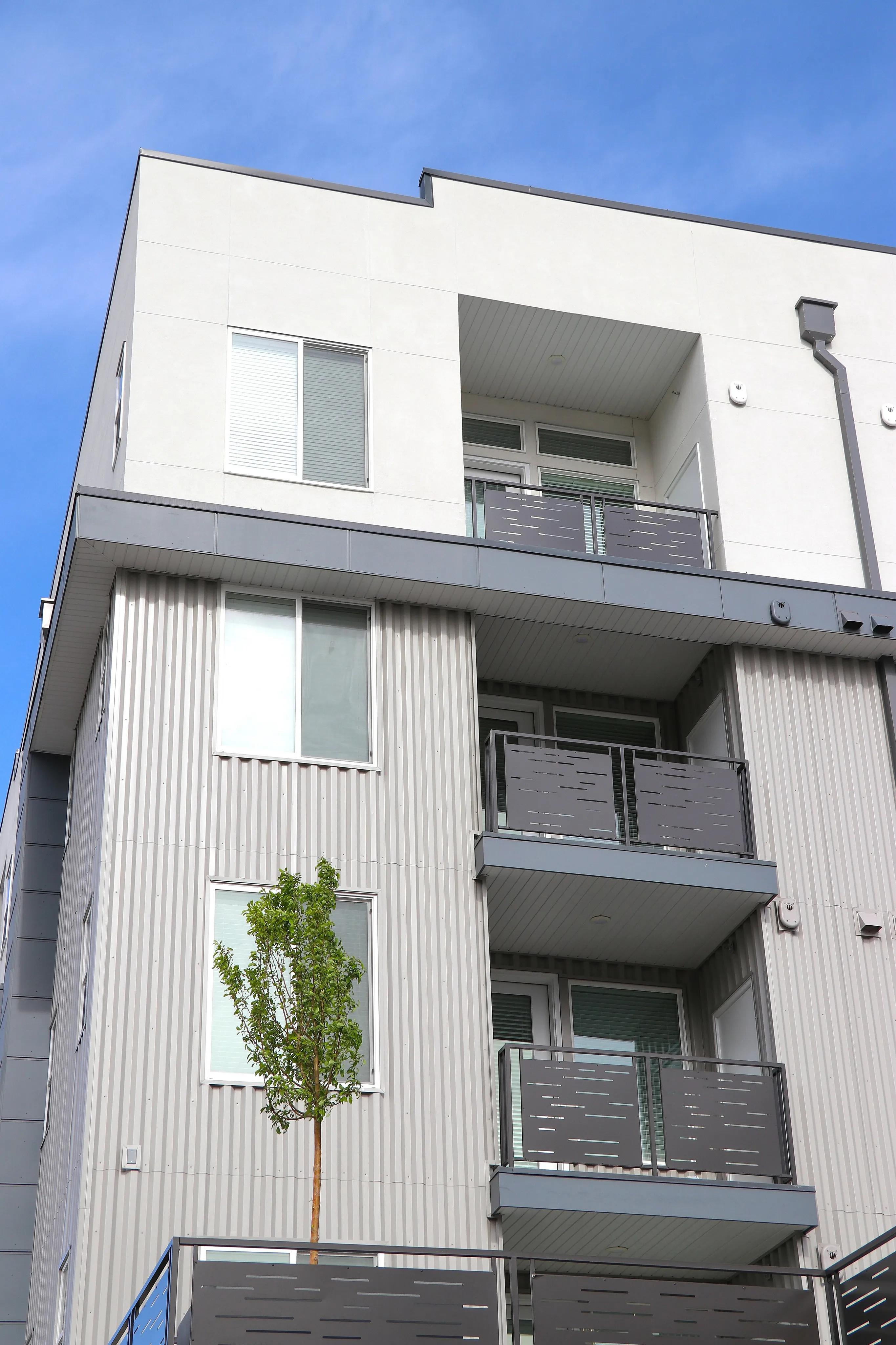 Modern apartment building with sleek balconies and large windows against a clear blue sky, showcasing contemporary urban living.