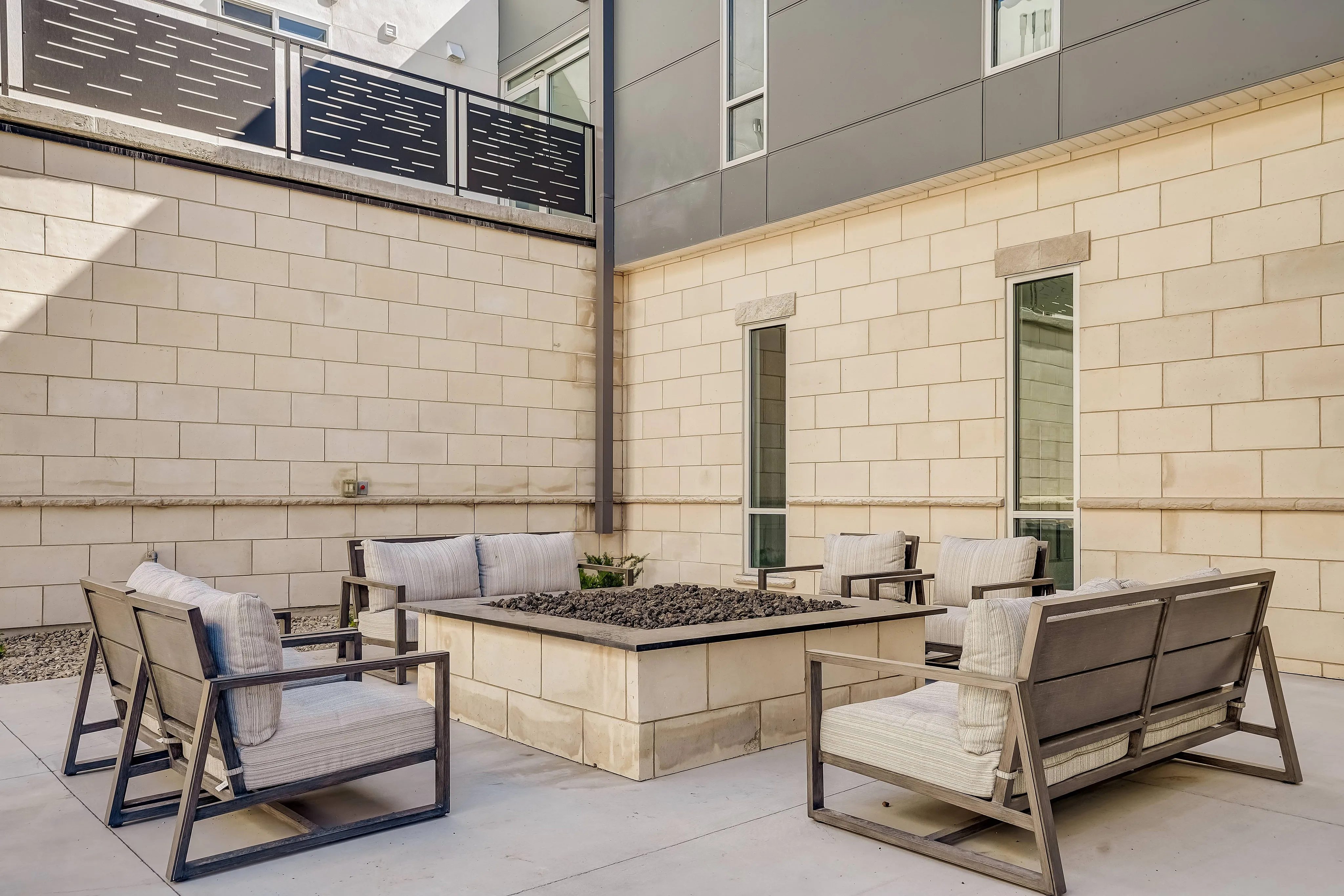 Chic outdoor patio with modern seating and a central fire pit, framed by stylish beige brick walls.