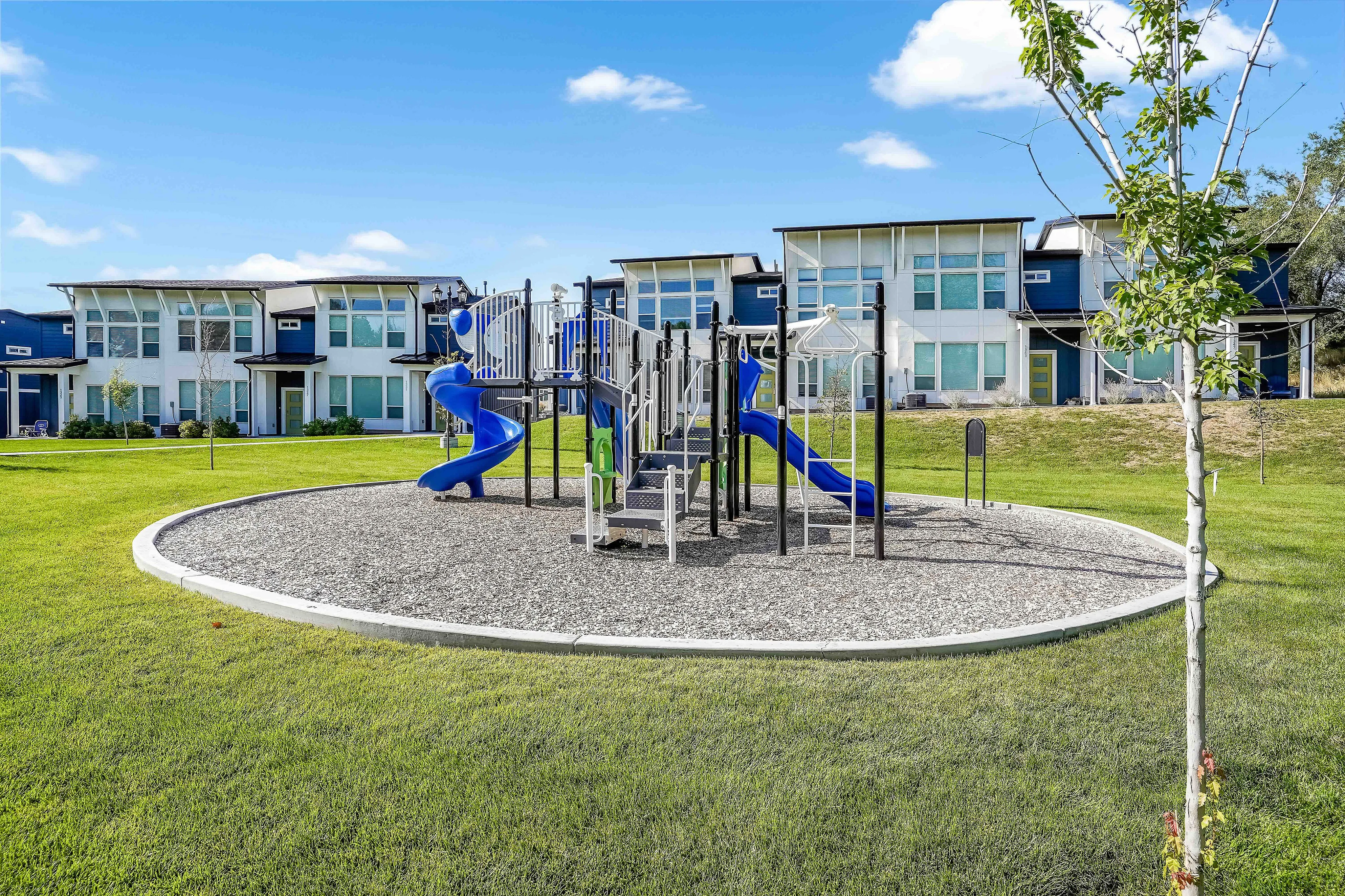 Charming residential community with modern townhouses and a vibrant playground, set against a clear blue sky.