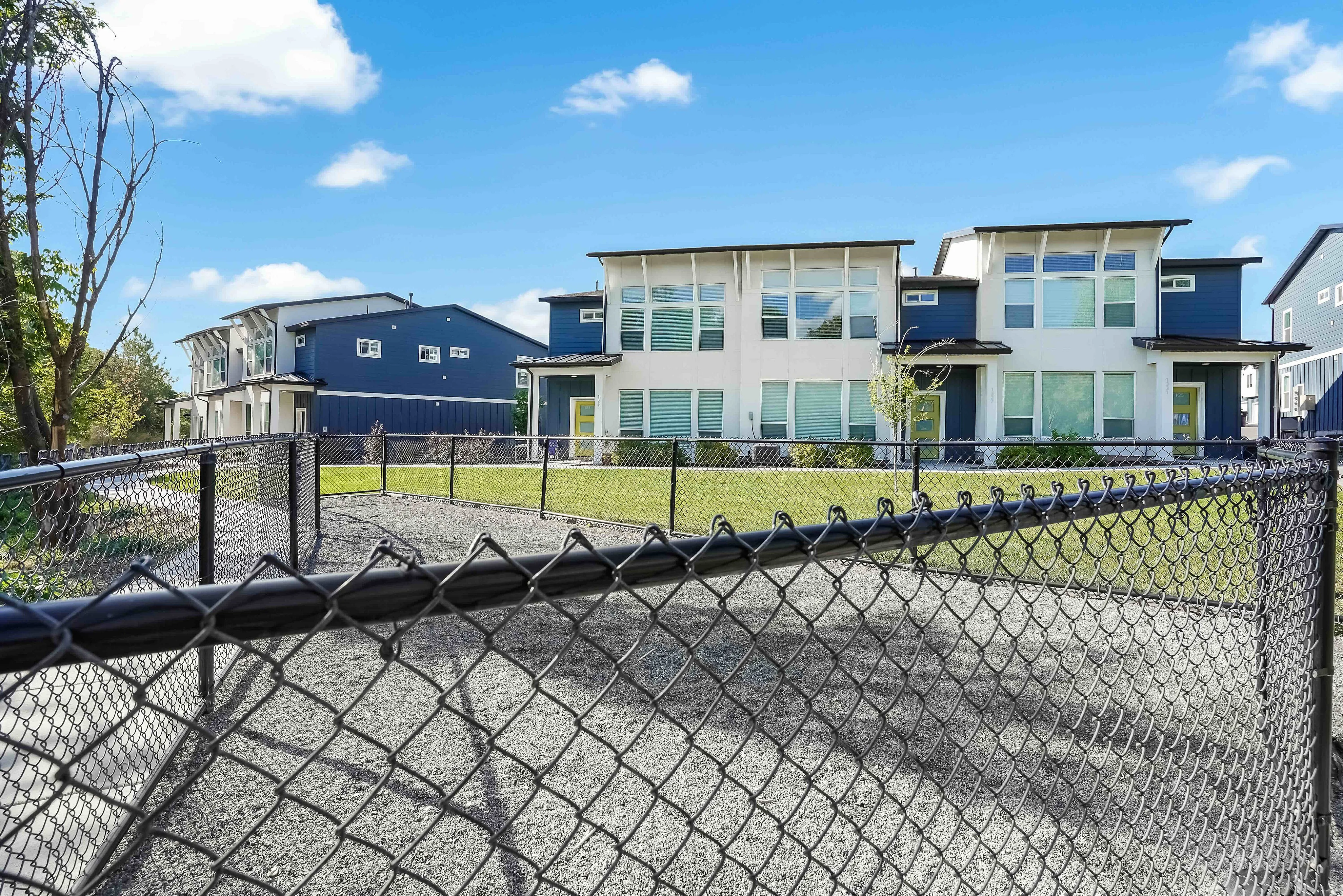 Modern two-story homes with expansive windows, nestled behind a secure fence, basking in a bright sunny day.