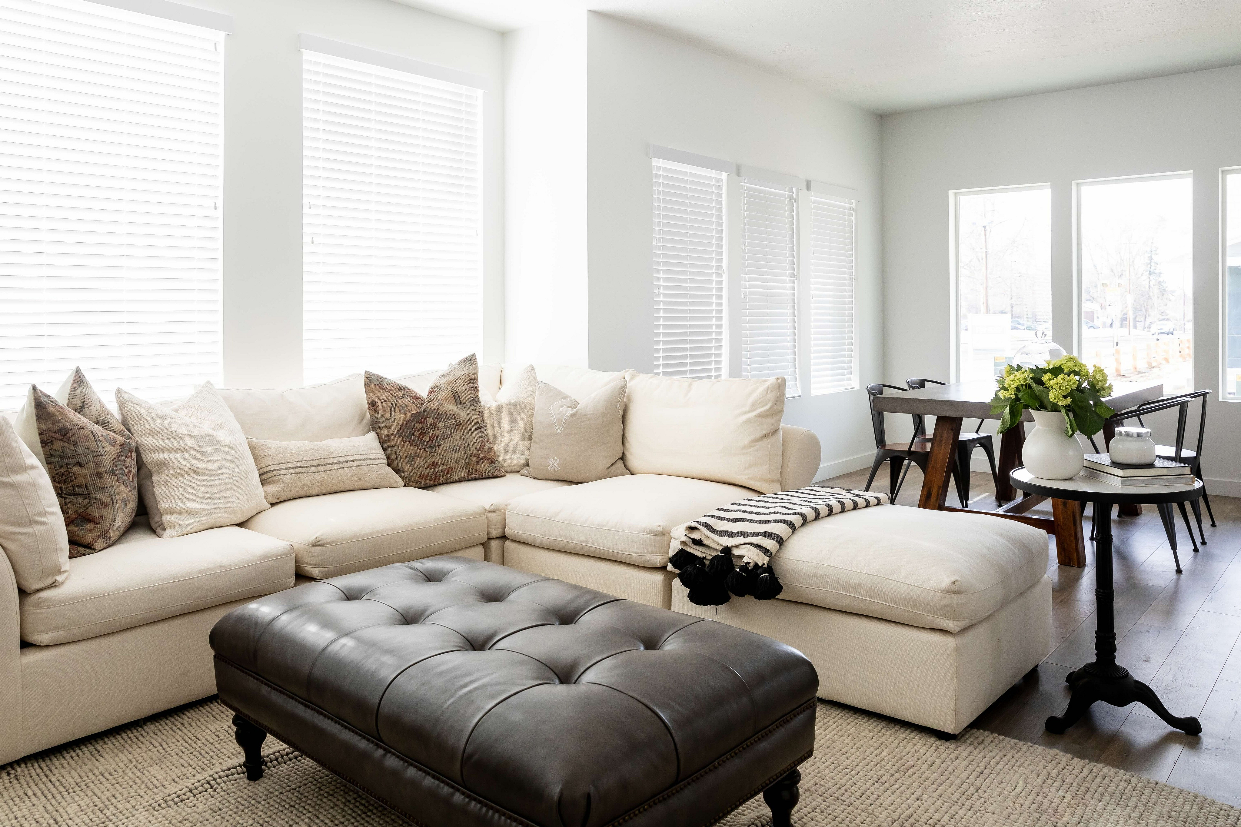 Bright and inviting living space featuring a cozy cream sectional, stylish dark leather ottoman, and elegant dining area with modern accents.