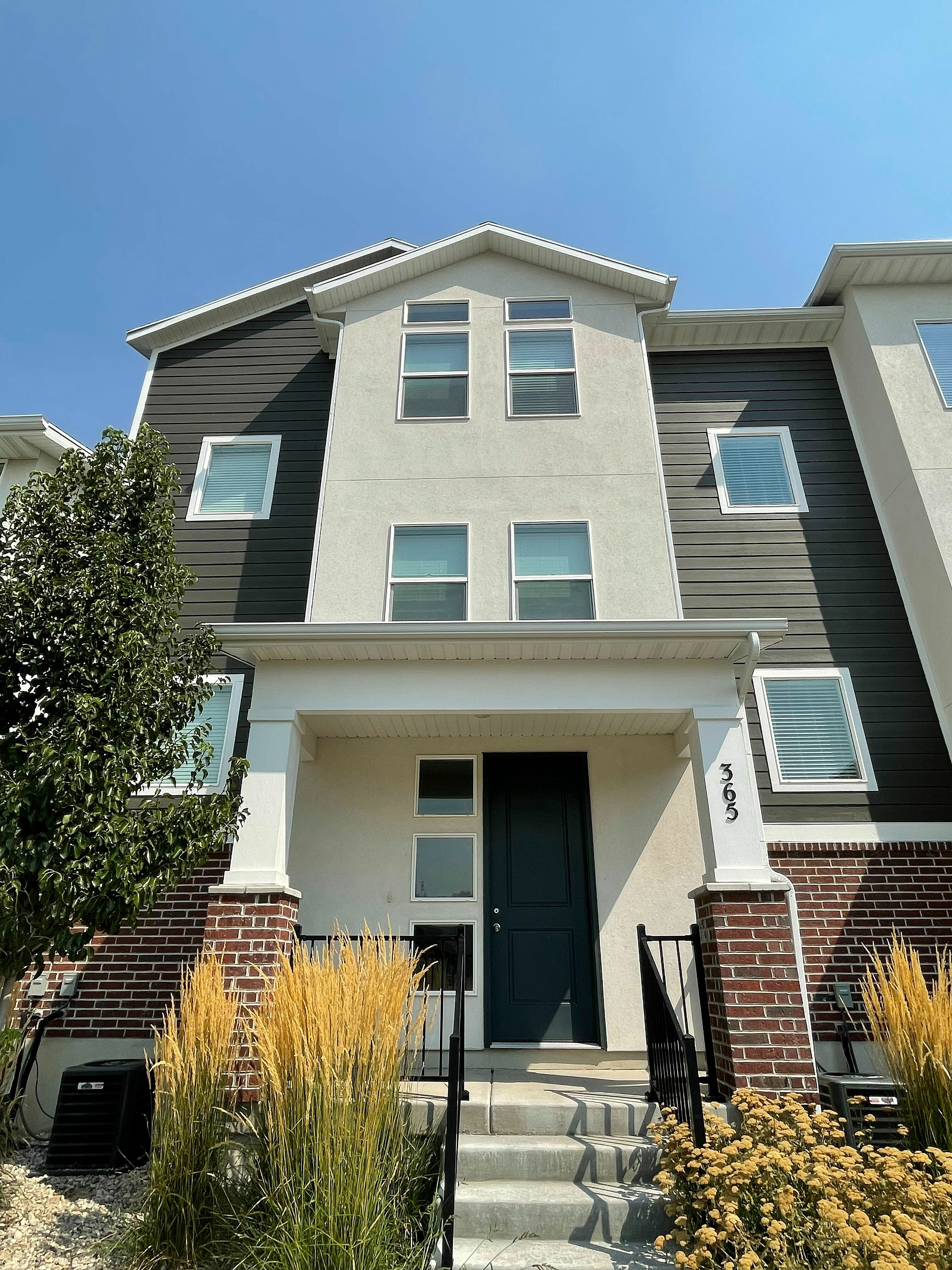 Charming modern townhouse with sleek architectural design, a welcoming entrance, and stylish landscaping under a clear blue sky.