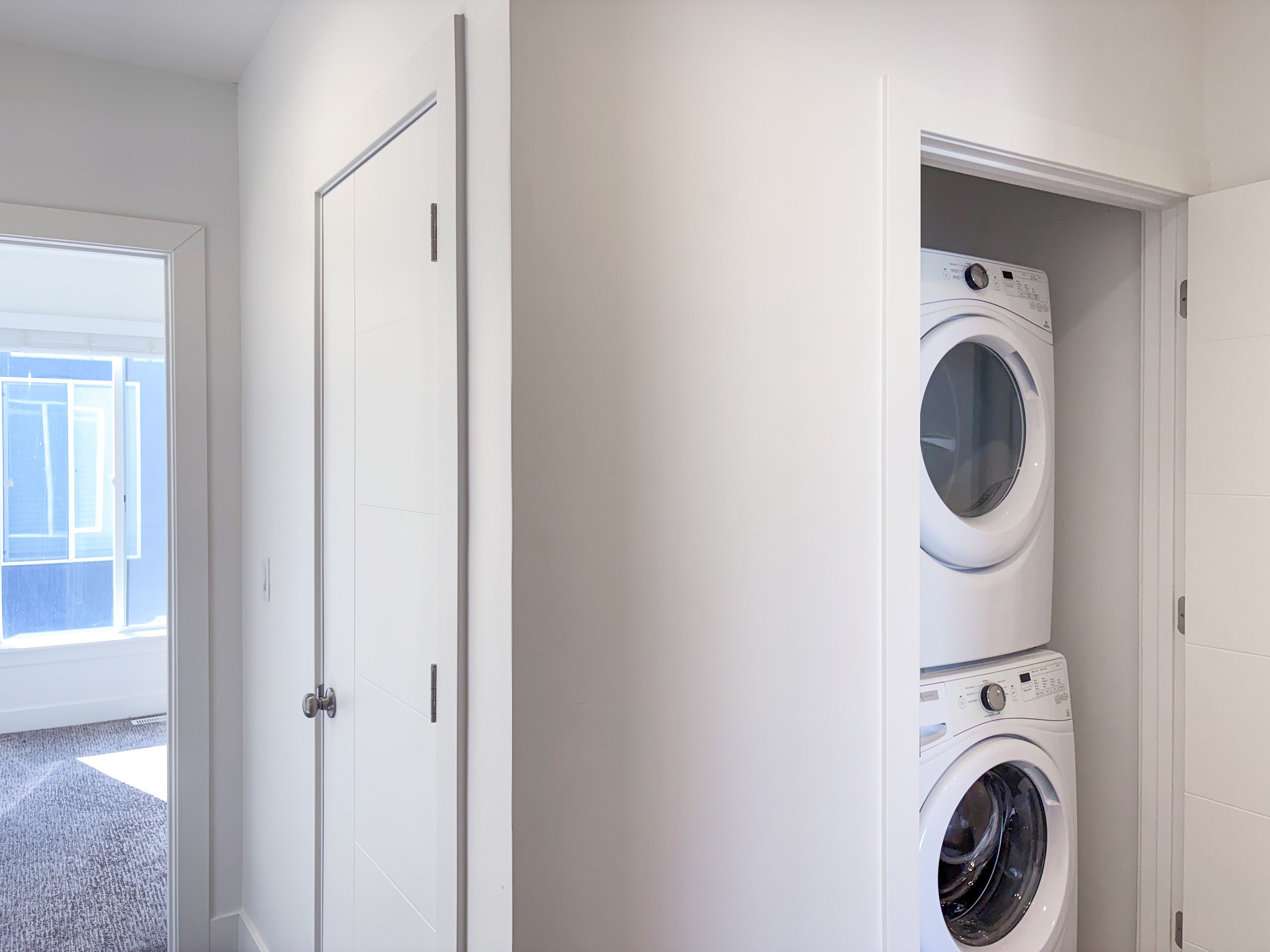 Bright apartment corridor featuring a convenient stacked washer and dryer closet with sunlight streaming through a nearby window.