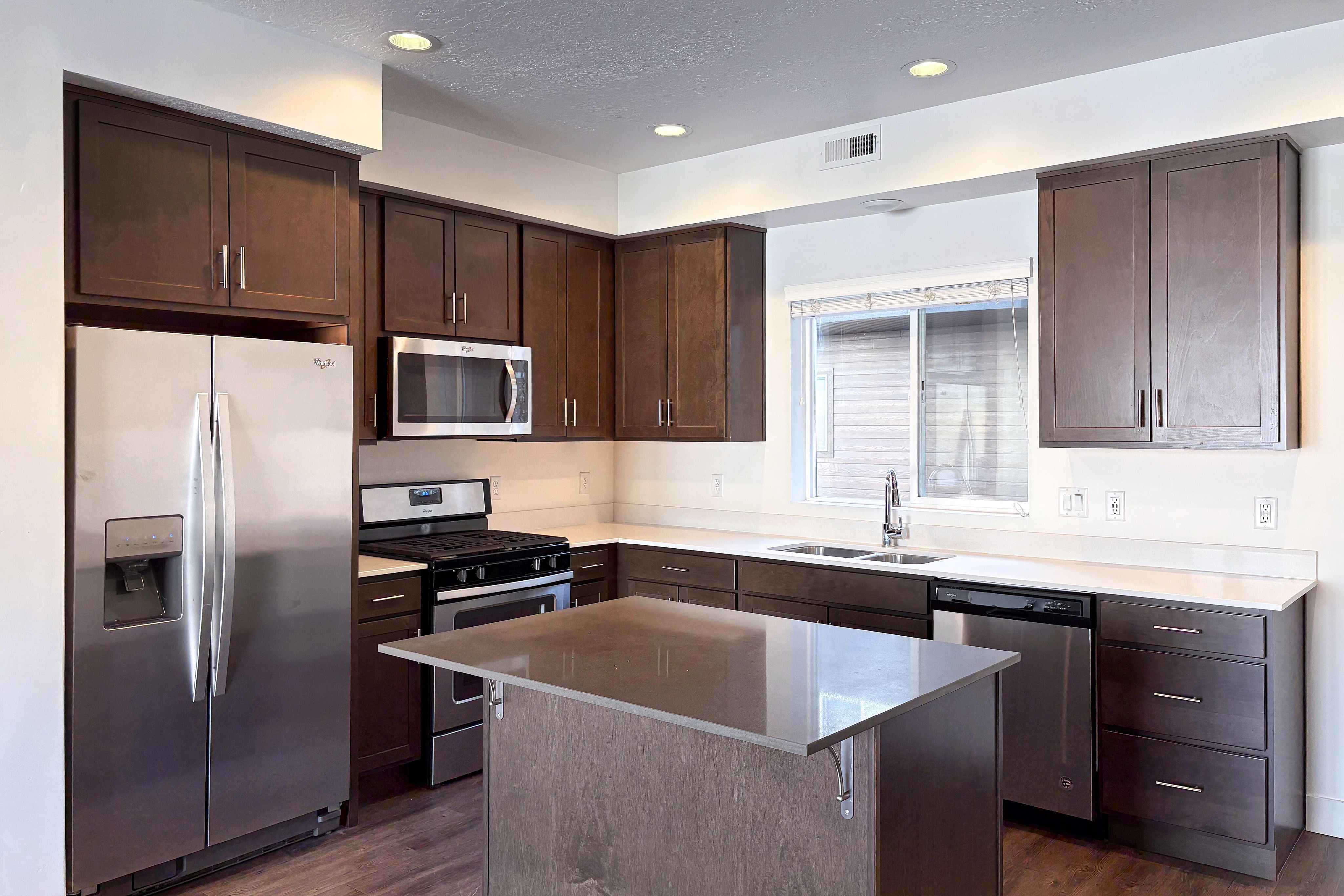 Modern kitchen design with sleek stainless steel appliances, rich dark wood cabinets, and a spacious island counter under elegant recessed lighting.