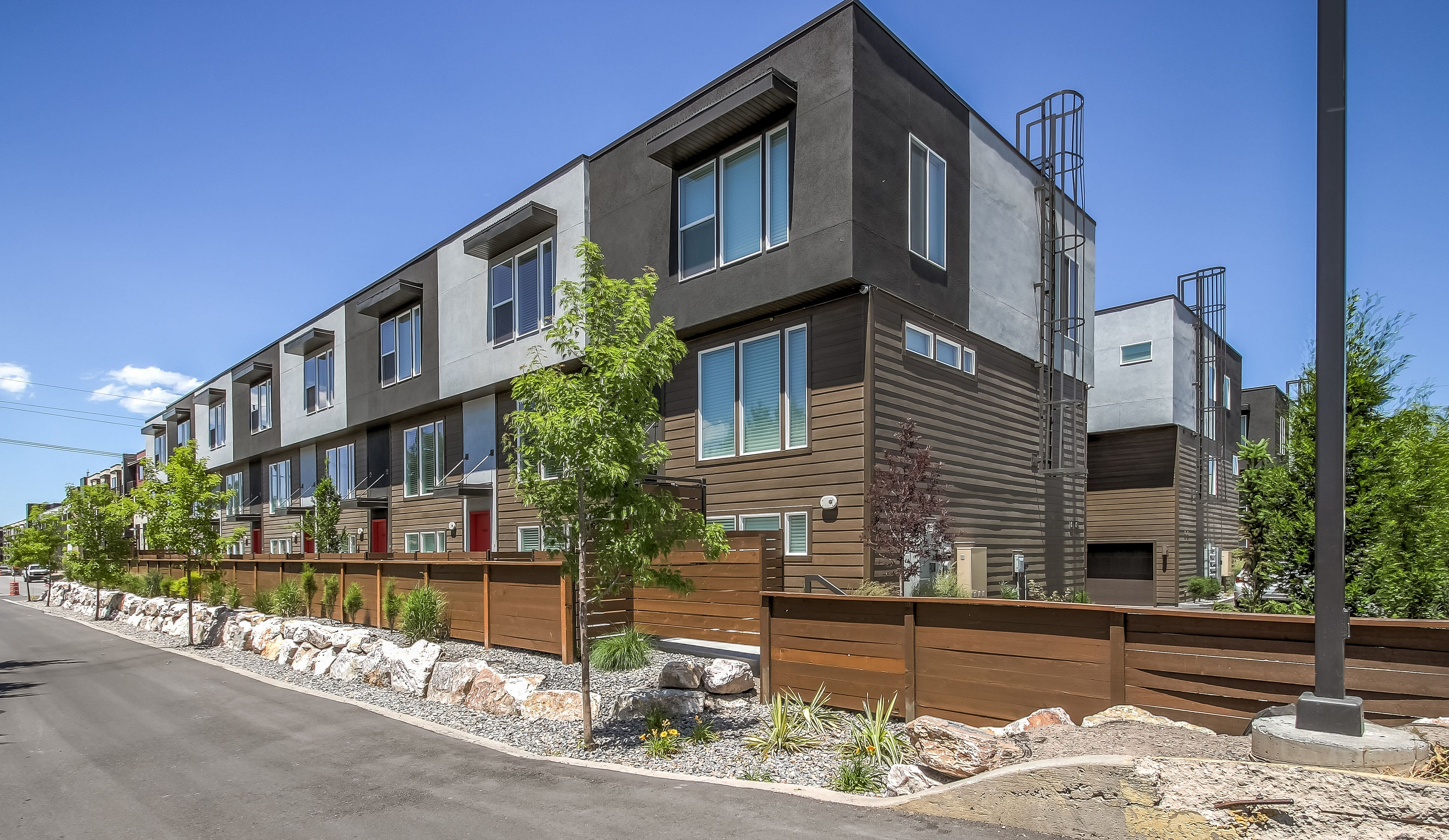 Modern townhouse complex with sleek architecture, vibrant red doors, and well-maintained landscaping under a clear blue sky.