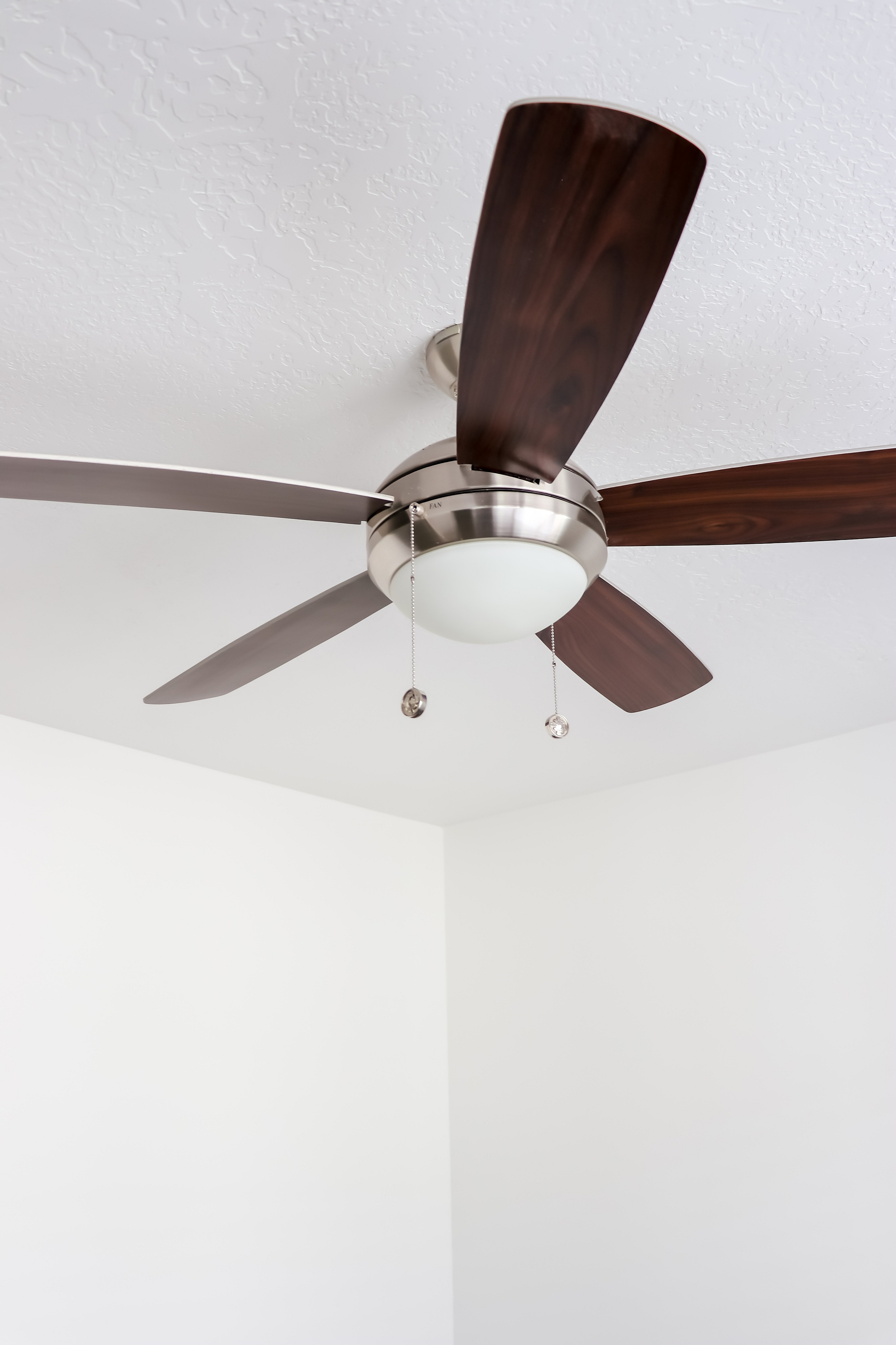 Elegant modern ceiling fan with sleek wooden blades adds style to a bright, minimalistic room.