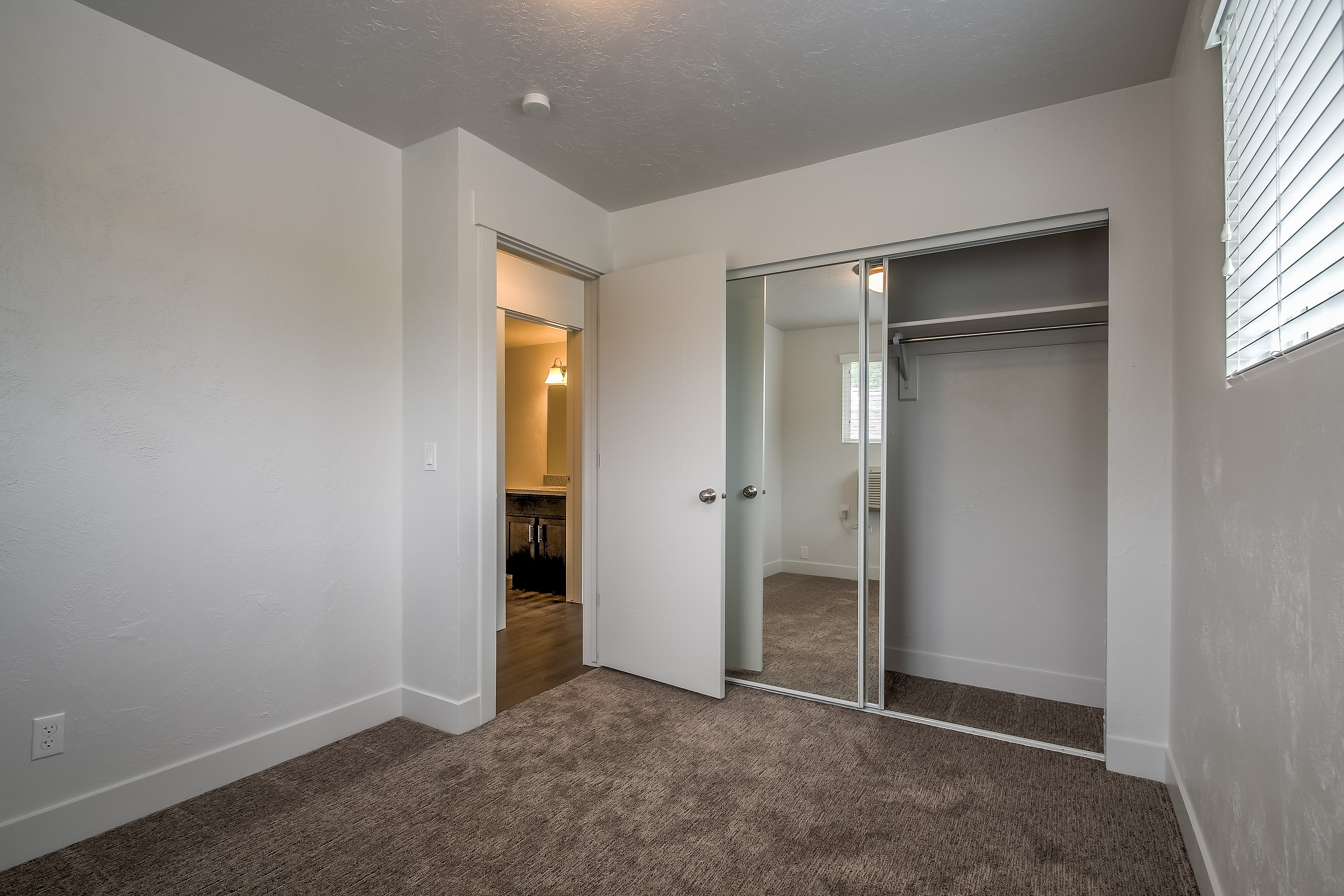 Bright bedroom with plush carpet, mirrored closet doors, and a view into a well-lit bathroom. Perfect blend of comfort and style.