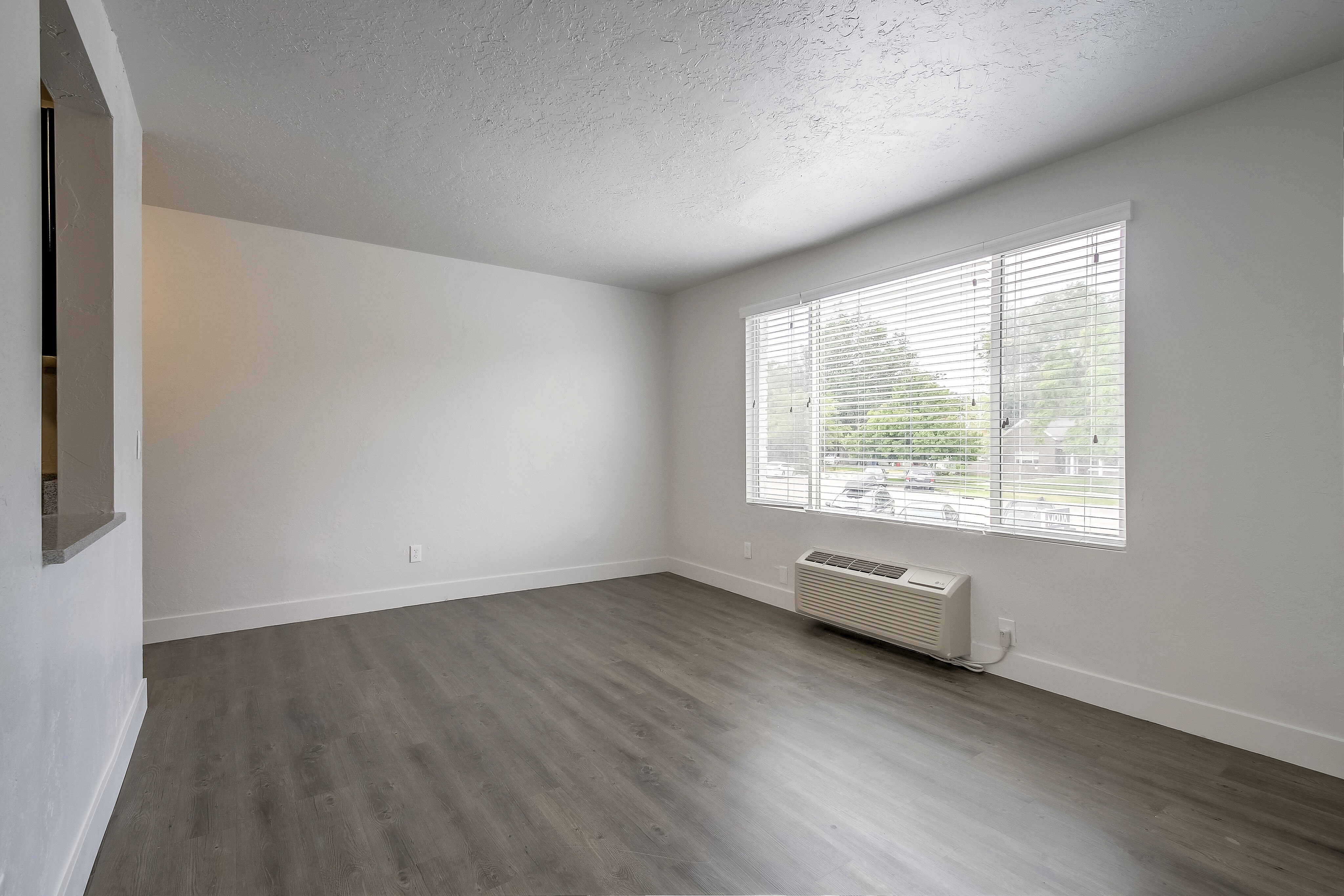 Bright and airy room with elegant wood flooring, large windows providing abundant natural light, and a serene view of lush greenery.