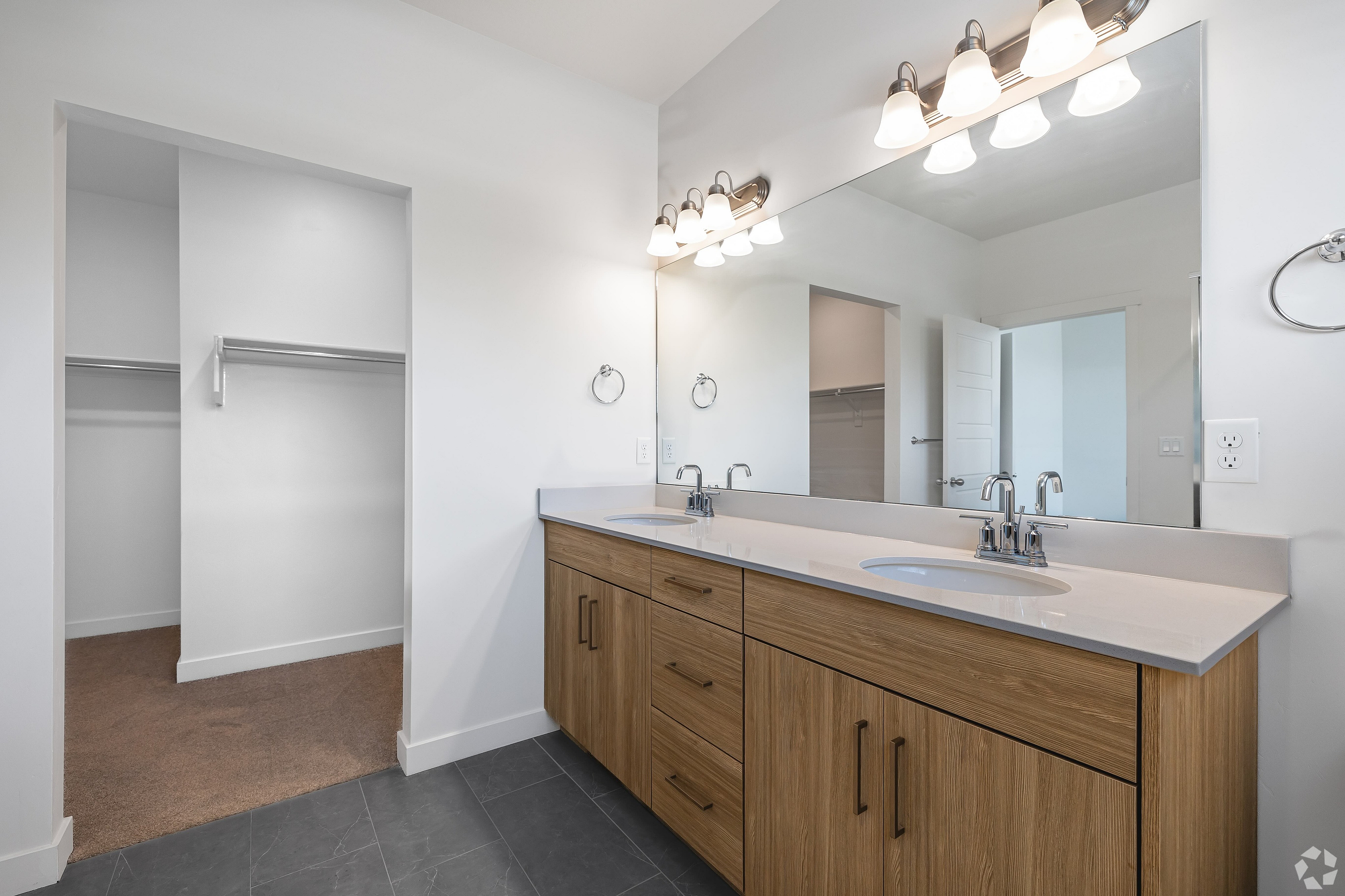 Modern bathroom features a double sink vanity with sleek wooden cabinets, stylish lighting, and a spacious open closet.