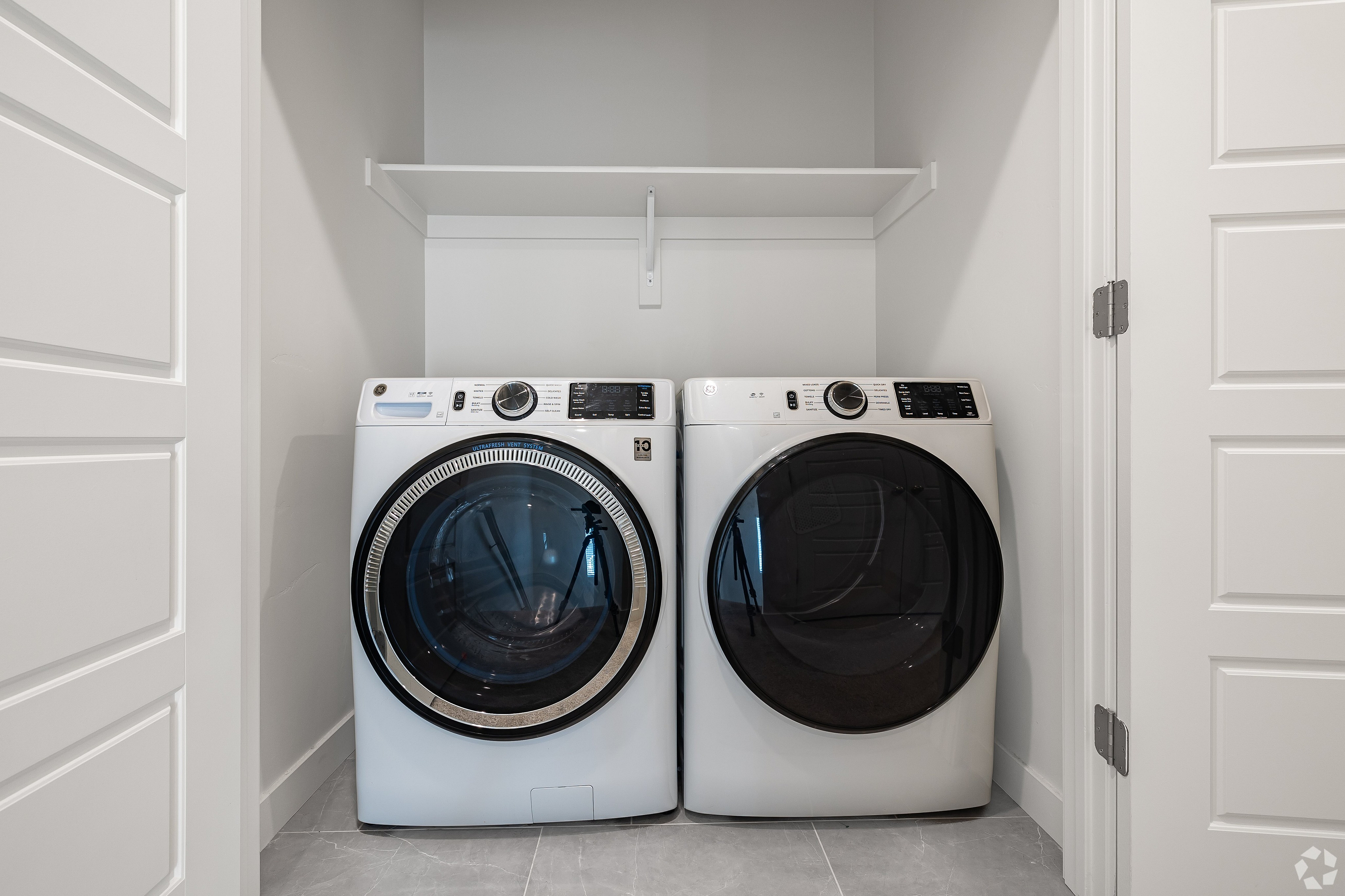 Modern and sleek laundry area with a matching front-loading washer and dryer set, complemented by a minimalist shelf, enhancing convenience in style.