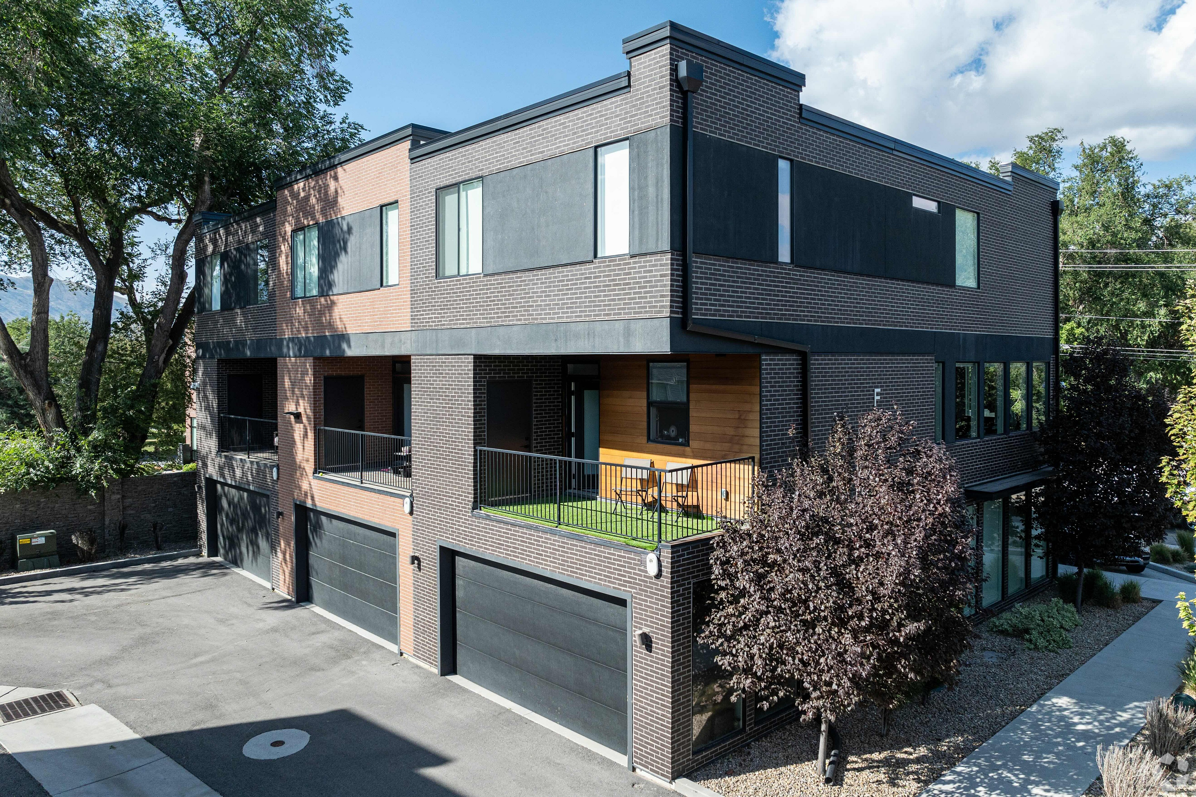Modern apartment building with sleek brick facade, private balconies, and surrounded by trees, offering a blend of urban style and natural beauty.