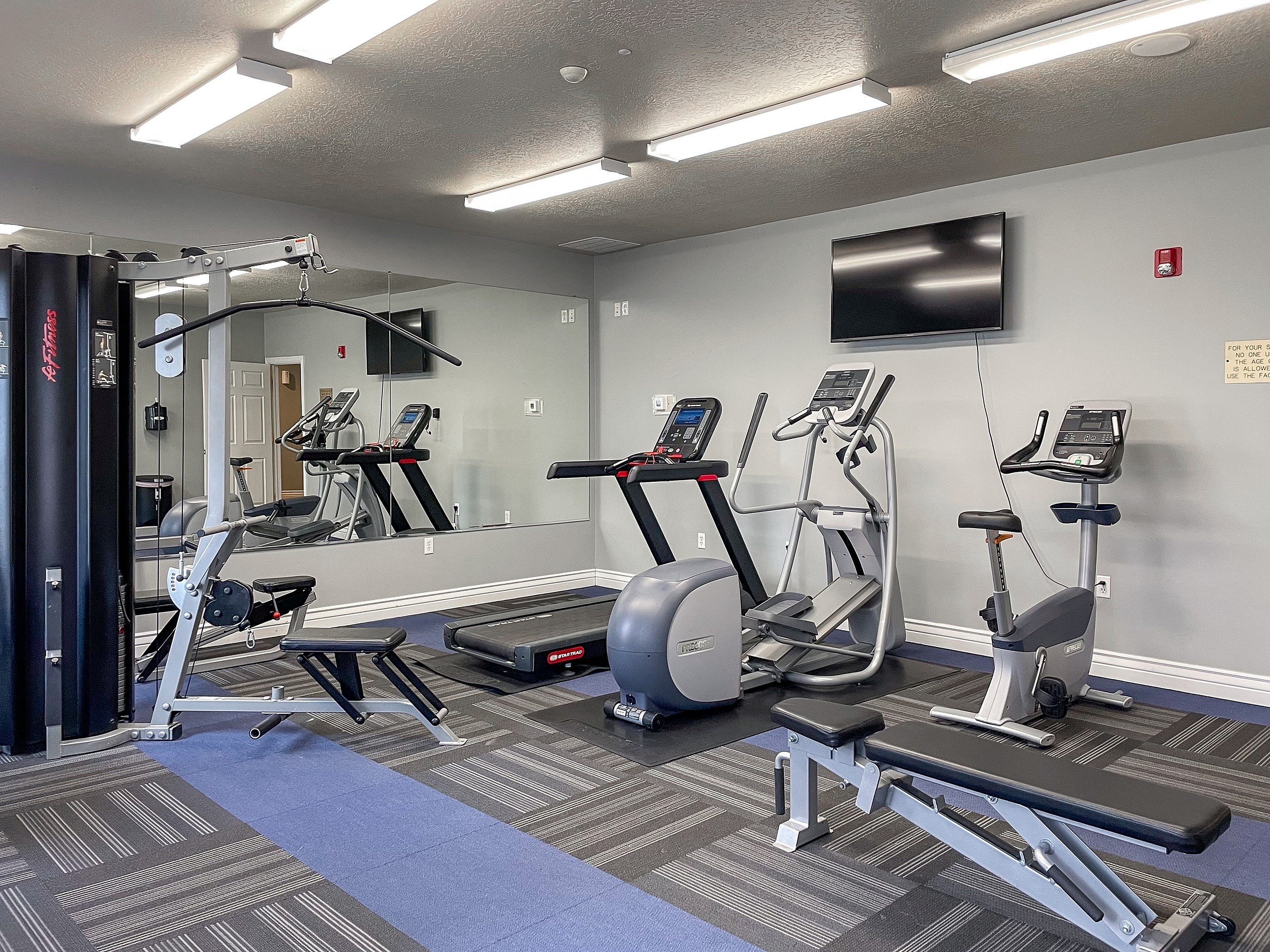 Modern fitness center with state-of-the-art equipment including treadmills, exercise bikes, and weight machines in a well-lit, spacious room.