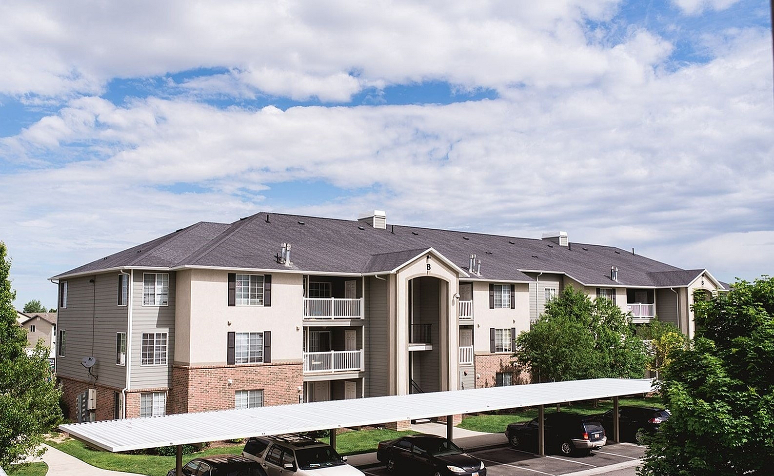 Charming apartment complex with modern architecture, ample parking, and lush surroundings under a beautiful sky.