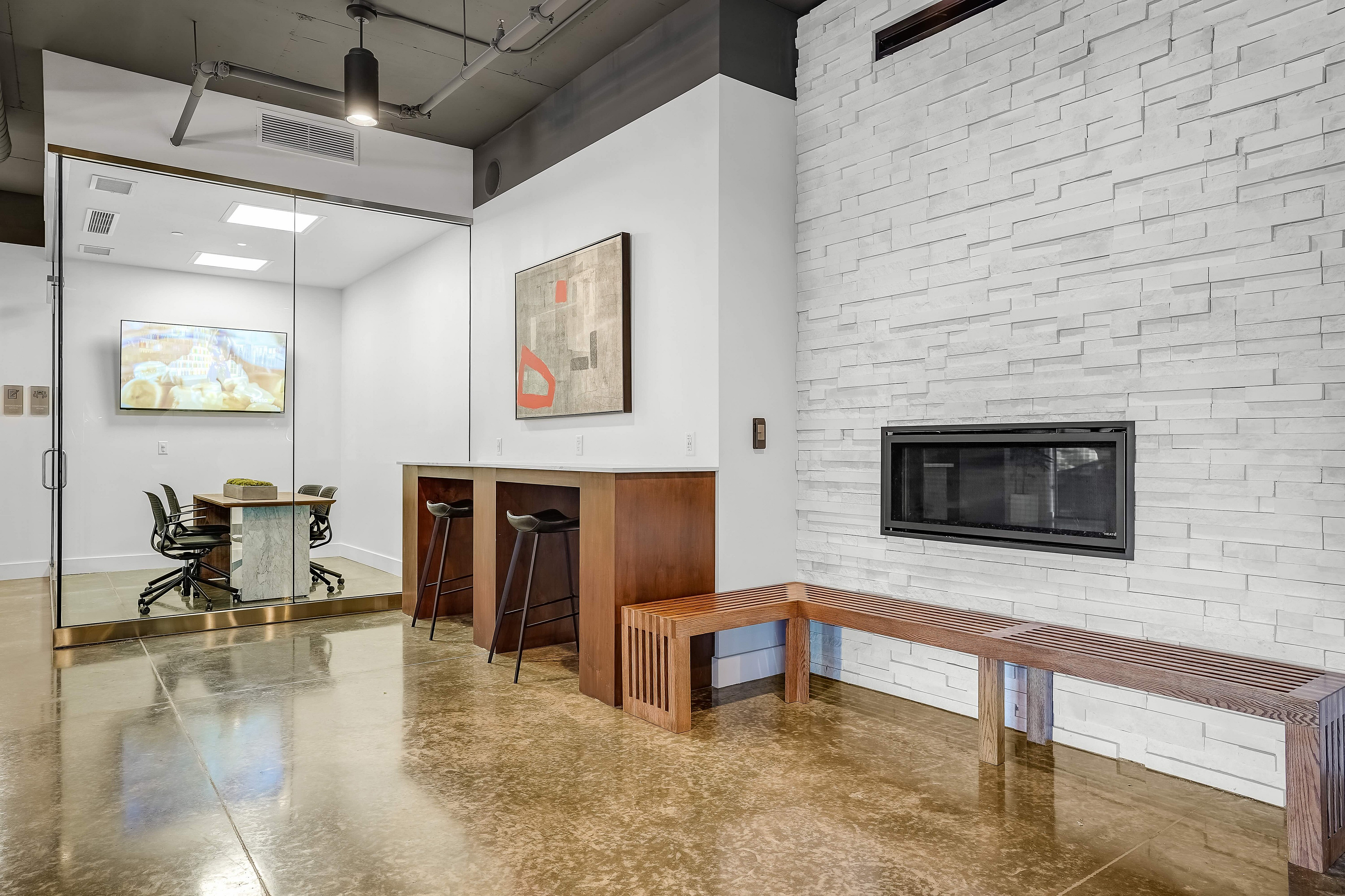 Modern office space featuring a sleek glass meeting room, stylish wooden furniture, and a contemporary white stone wall with a built-in fireplace.