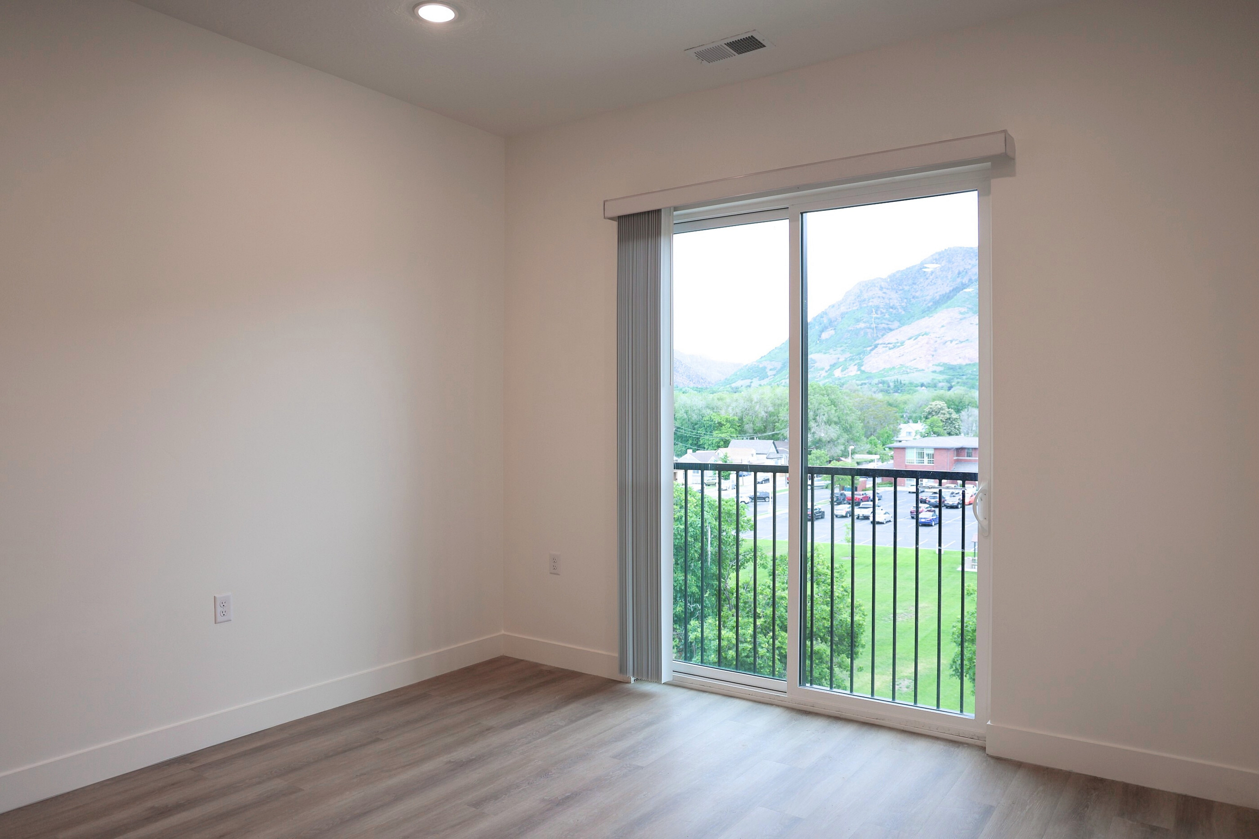 Bright, spacious apartment room with elegant hardwood floors and a large sliding glass door opening to a scenic mountain view.