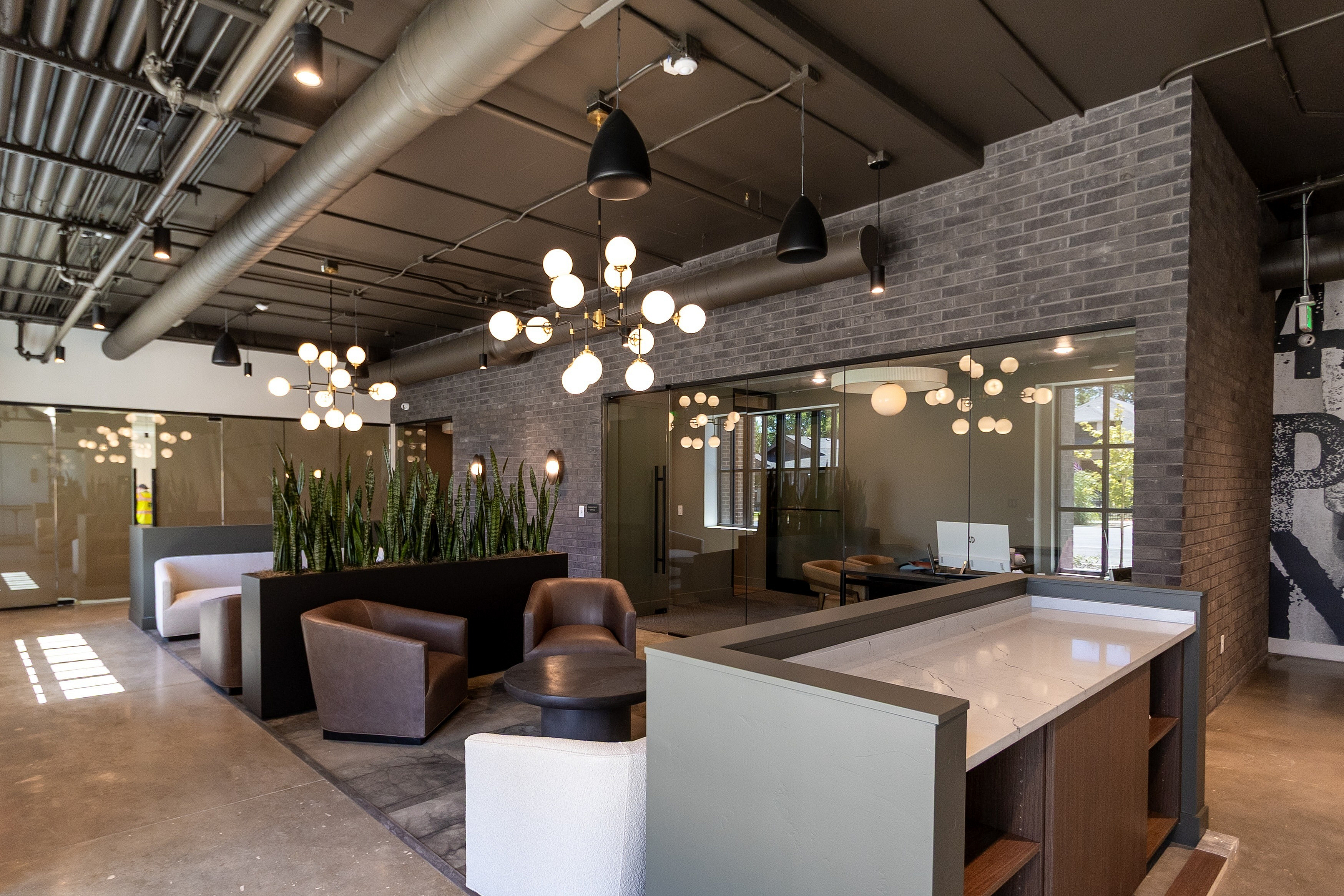 Modern office lounge with stylish lighting, comfortable seating, and sleek plants, creating an inviting workspace environment.