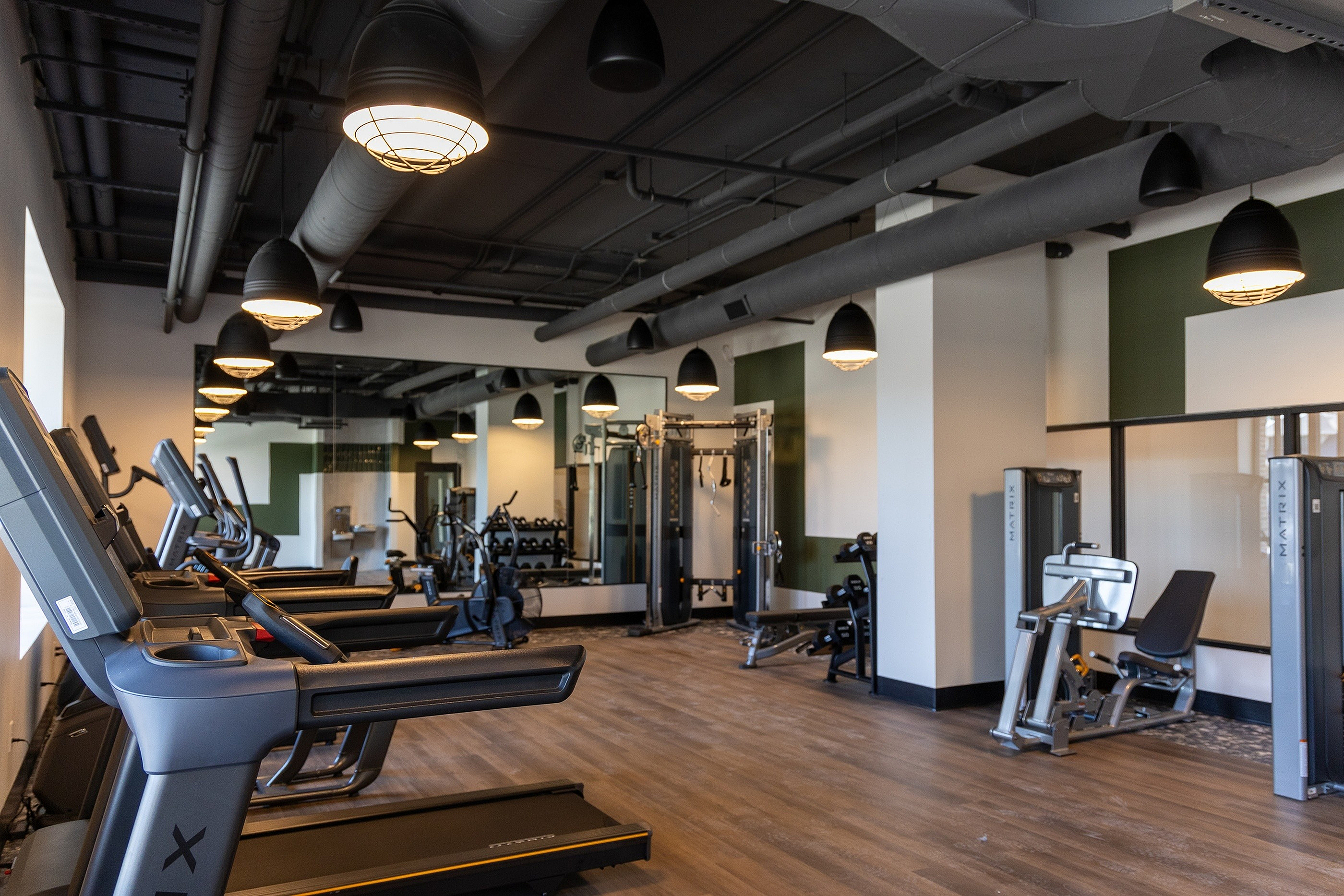 Modern fitness center with state-of-the-art equipment, treadmills, and strength training machines, surrounded by sleek industrial design and ample lighting.