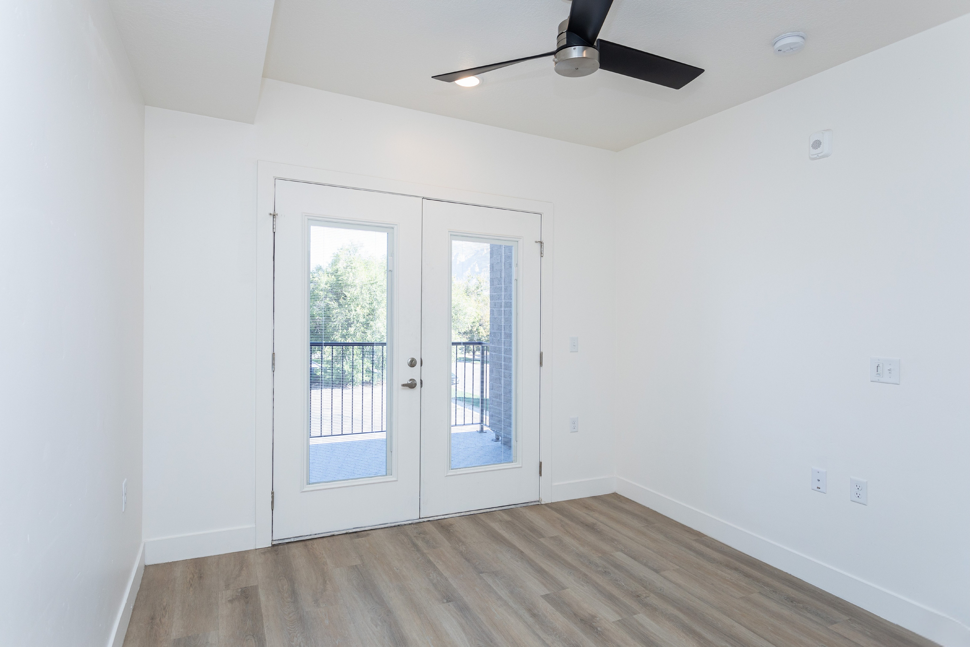 Bright room with elegant wood flooring and French doors leading to a scenic balcony, featuring a sleek ceiling fan and modern design.