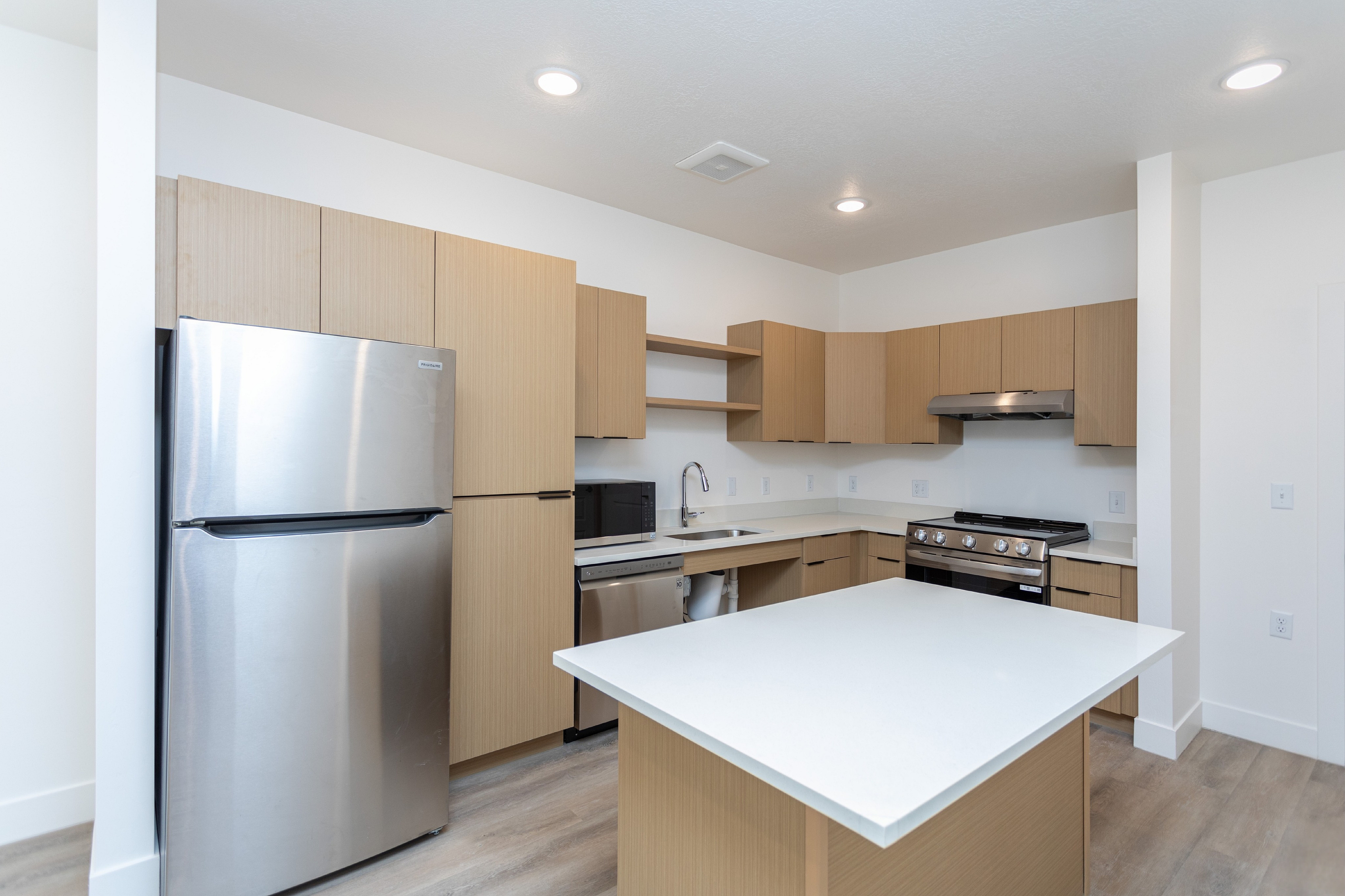 Modern kitchen with sleek stainless steel appliances, light wood cabinetry, and a spacious white countertop island.