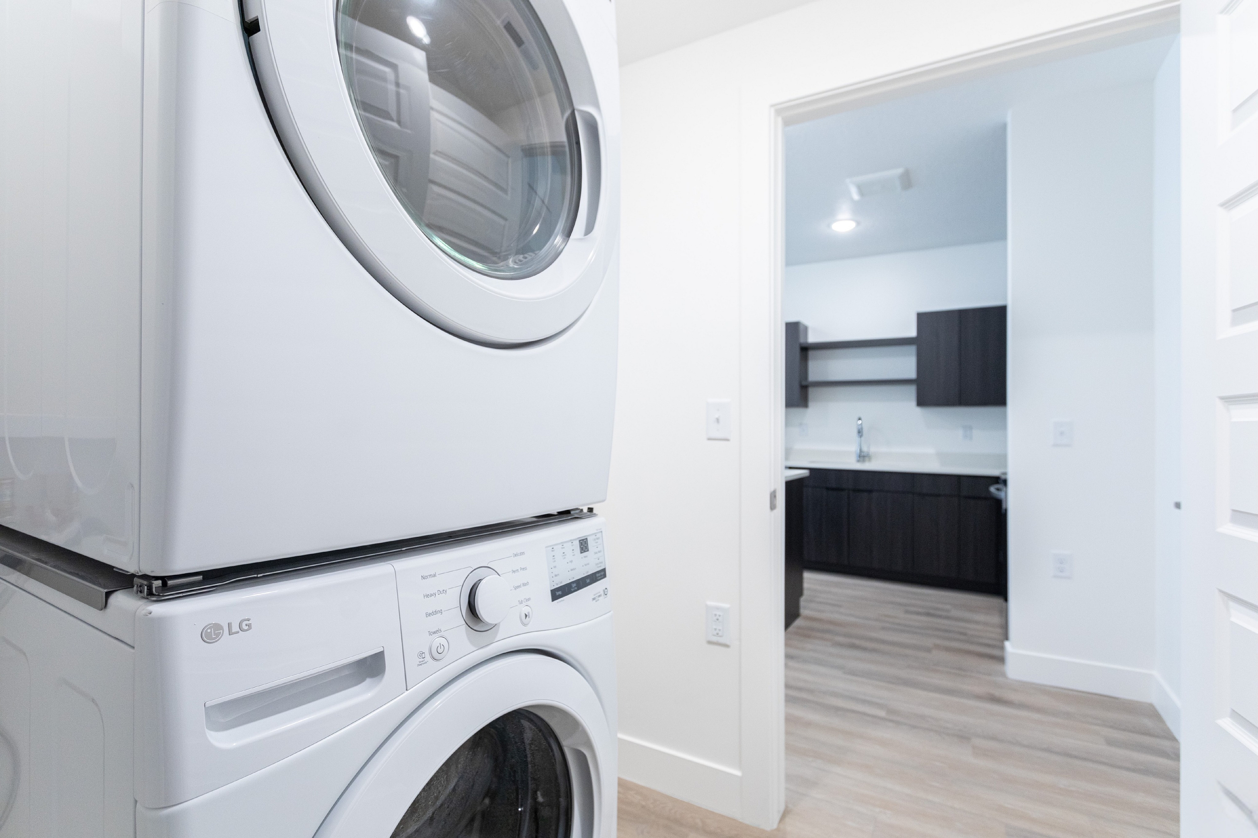 Modern apartment featuring a sleek LG washer and dryer set in a bright laundry area with hardwood floors, adjacent to a stylish contemporary kitchen.