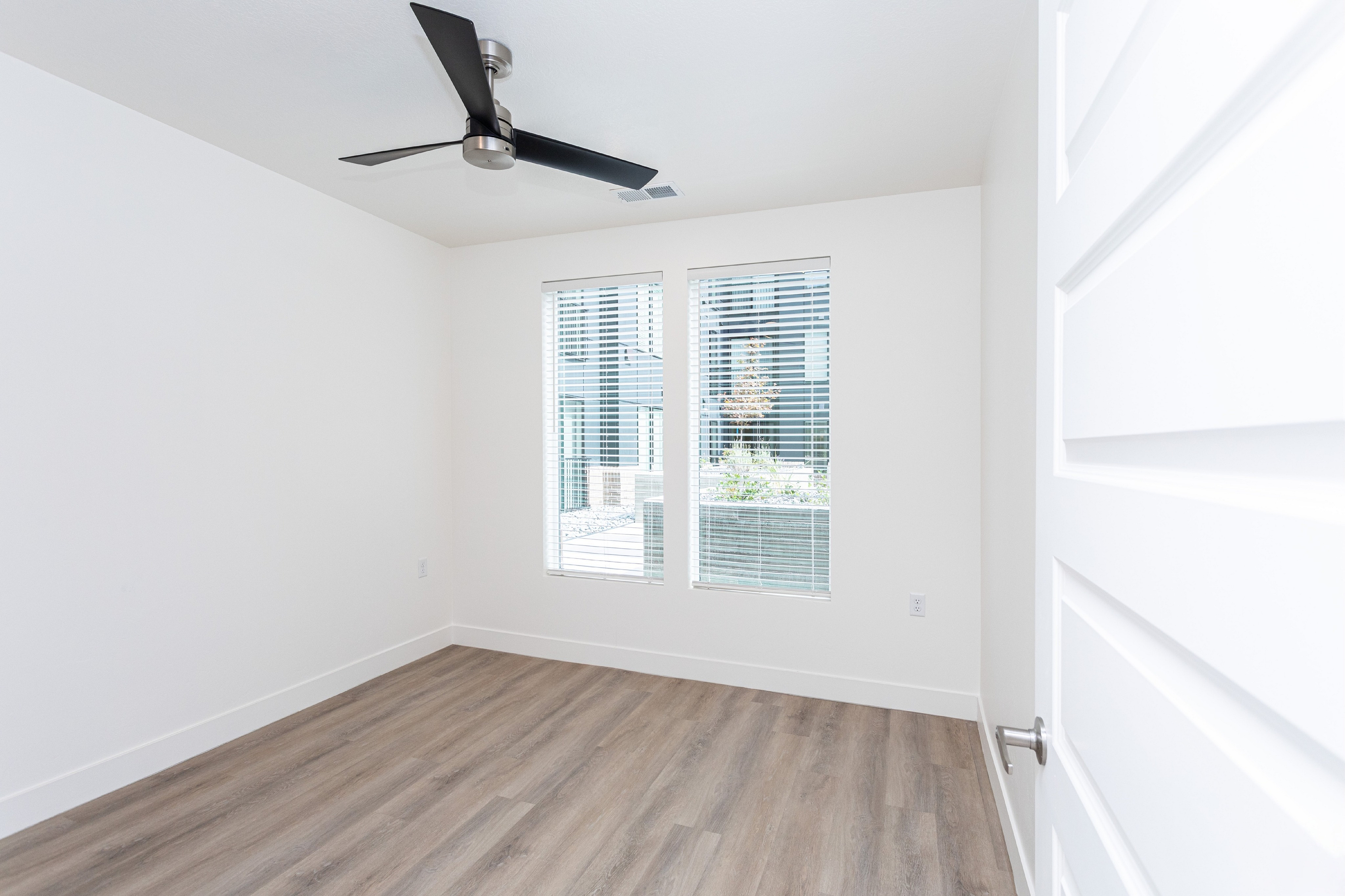 Bright and airy room with sleek wood flooring and modern ceiling fan, featuring large windows that invite natural light.