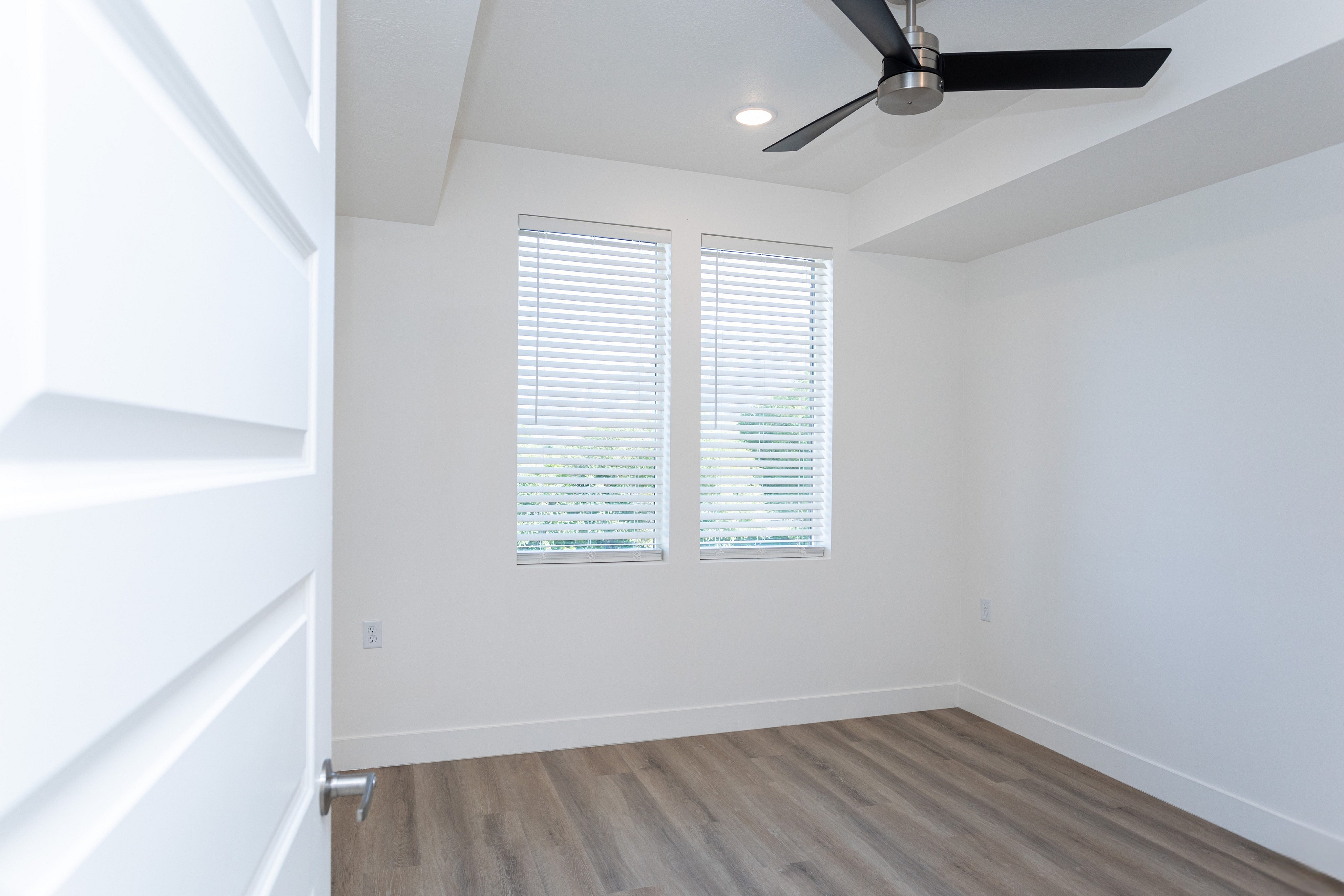 Bright and inviting room showcasing modern ceiling fan and large windows with blinds, perfect for a cozy living space.