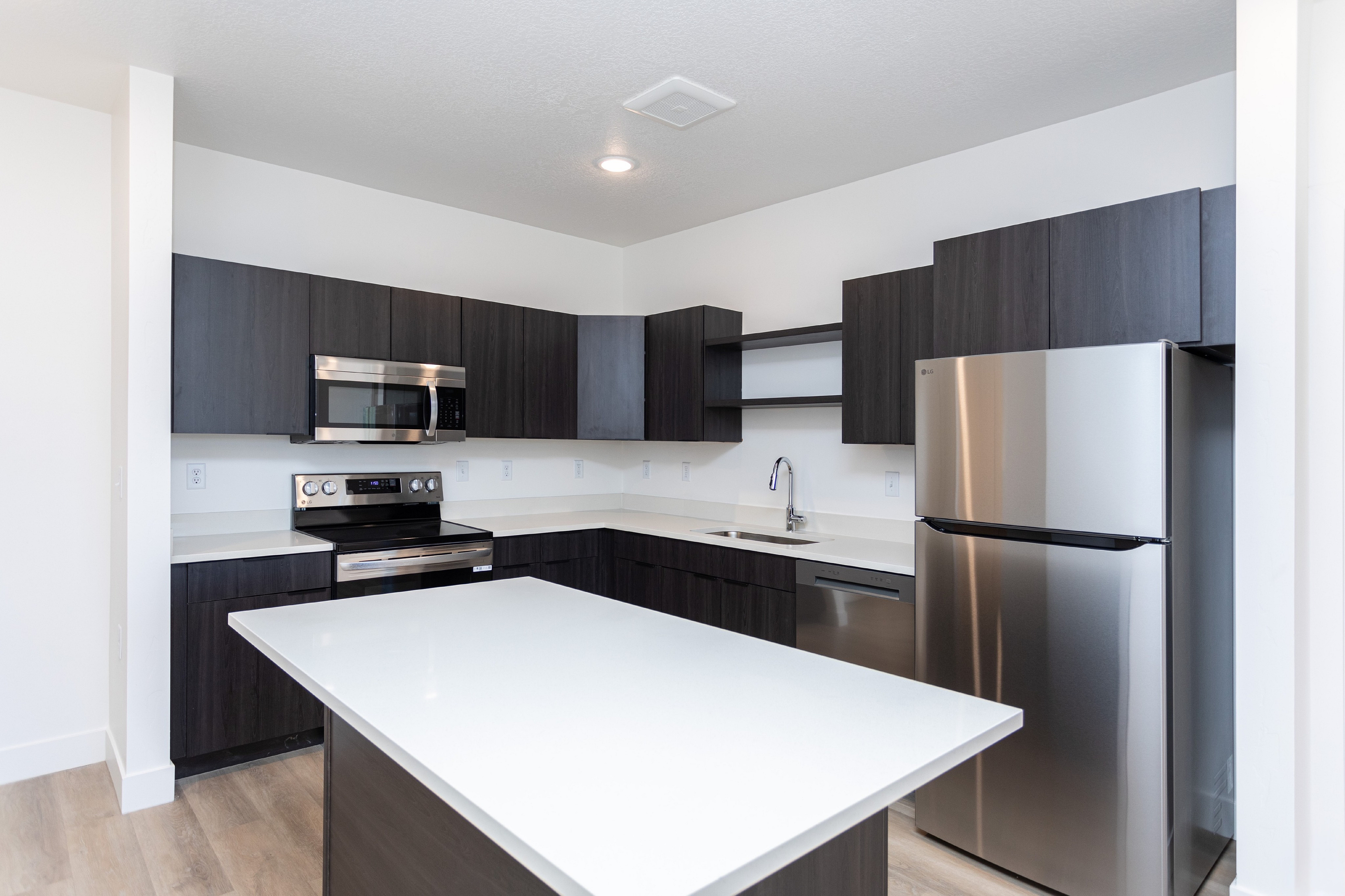 Contemporary kitchen with sleek dark cabinets, stainless steel appliances, and a large white countertop island.