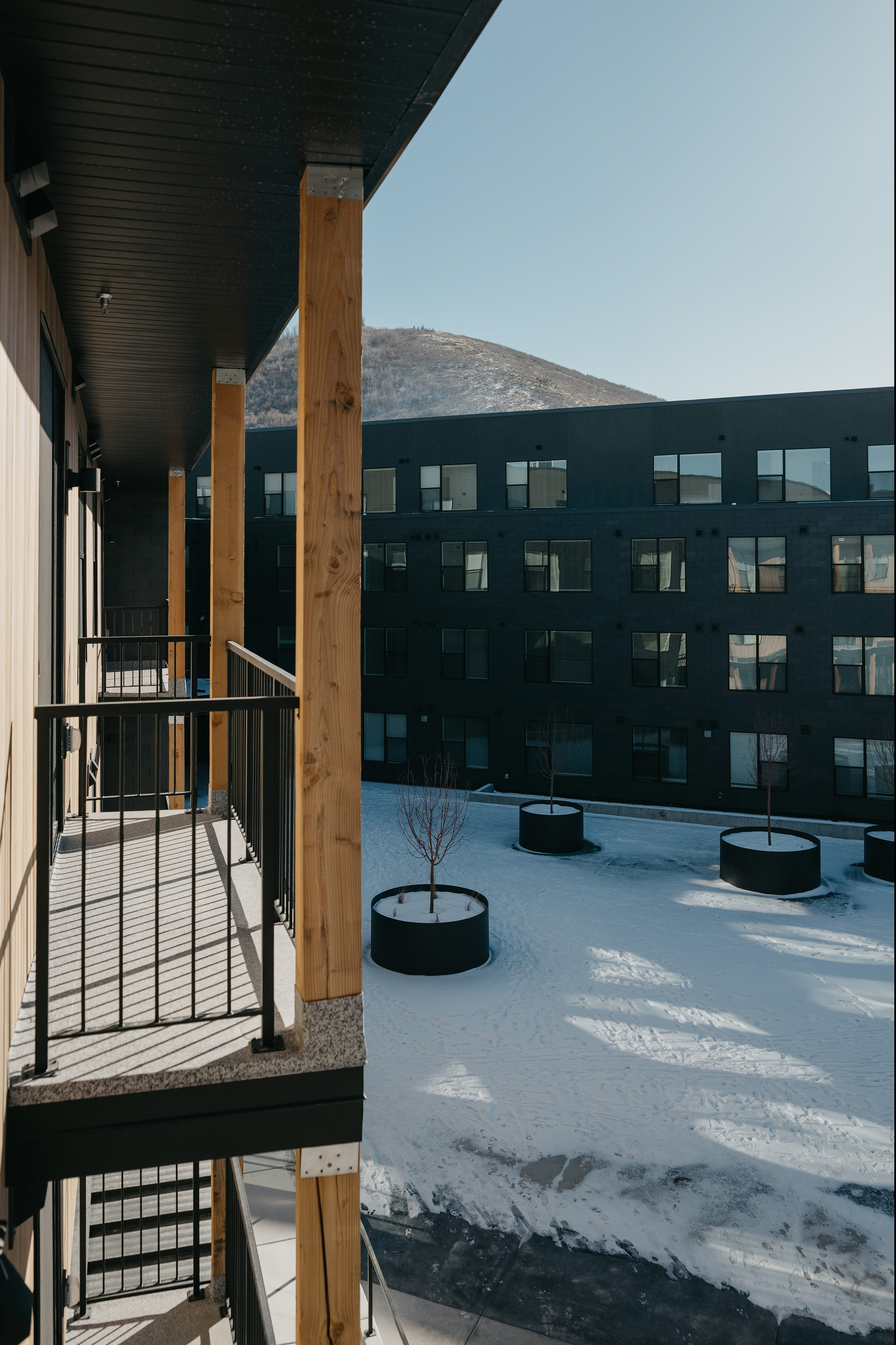 Chic apartment balcony with modern wood and metal design overlooking a scenic snow-covered courtyard and mountain view.